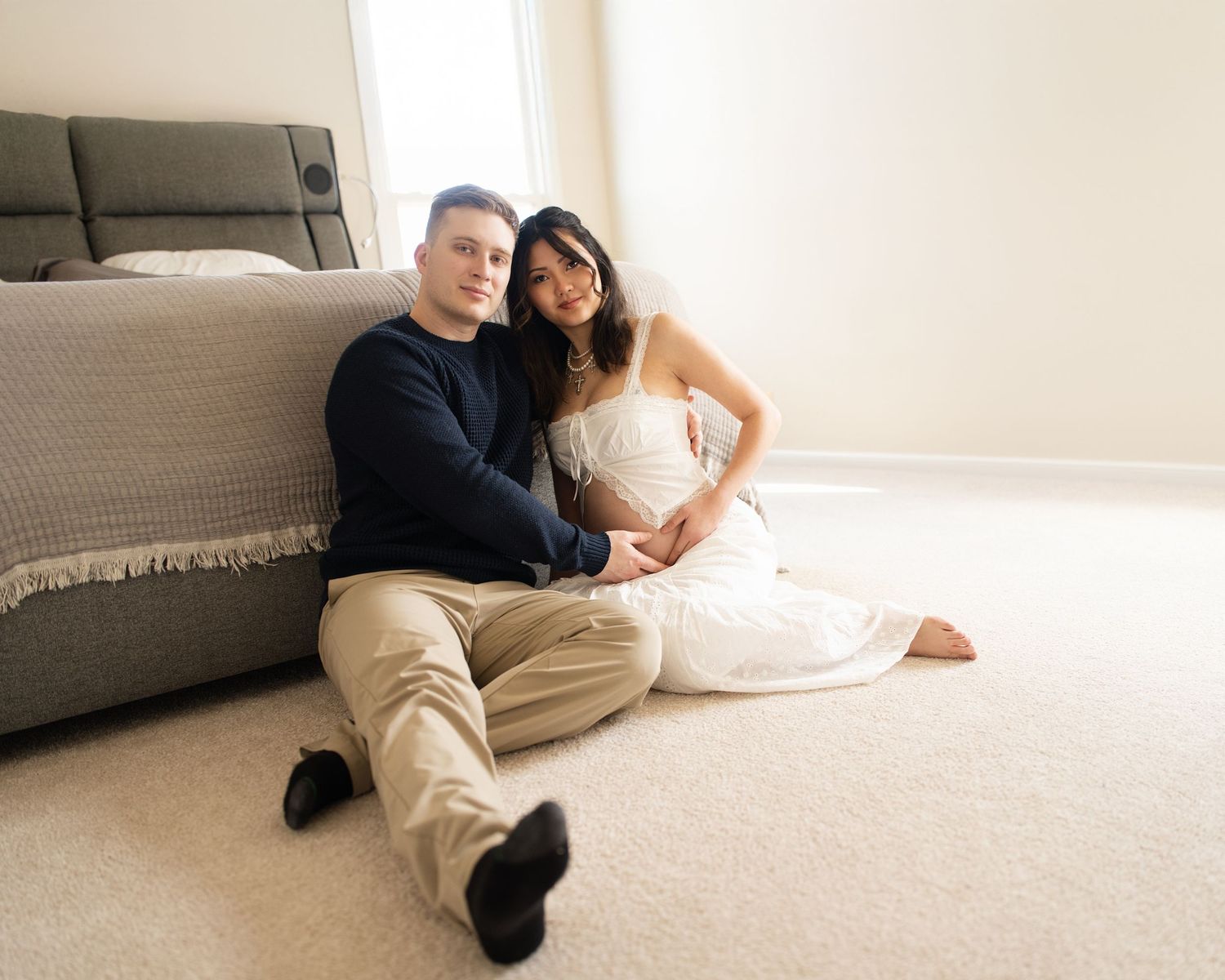 A couple in formal attire lies on a light carpet while looking at a mobile device together.
