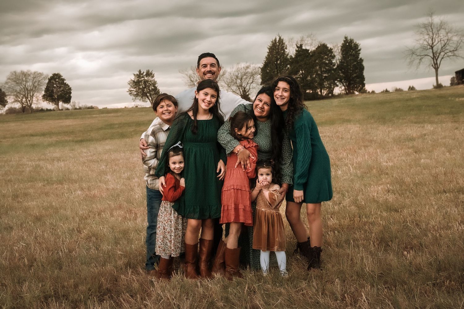 Family group poses together in a rustic outdoor field setting during golden hour.