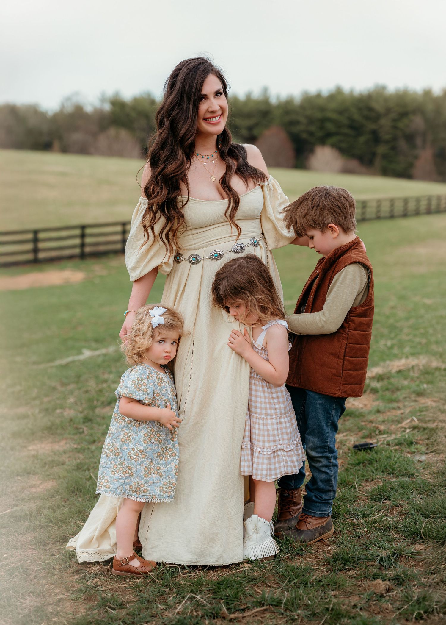 A family shares tender moments together on a grassy hillside with wooden fences in the background.