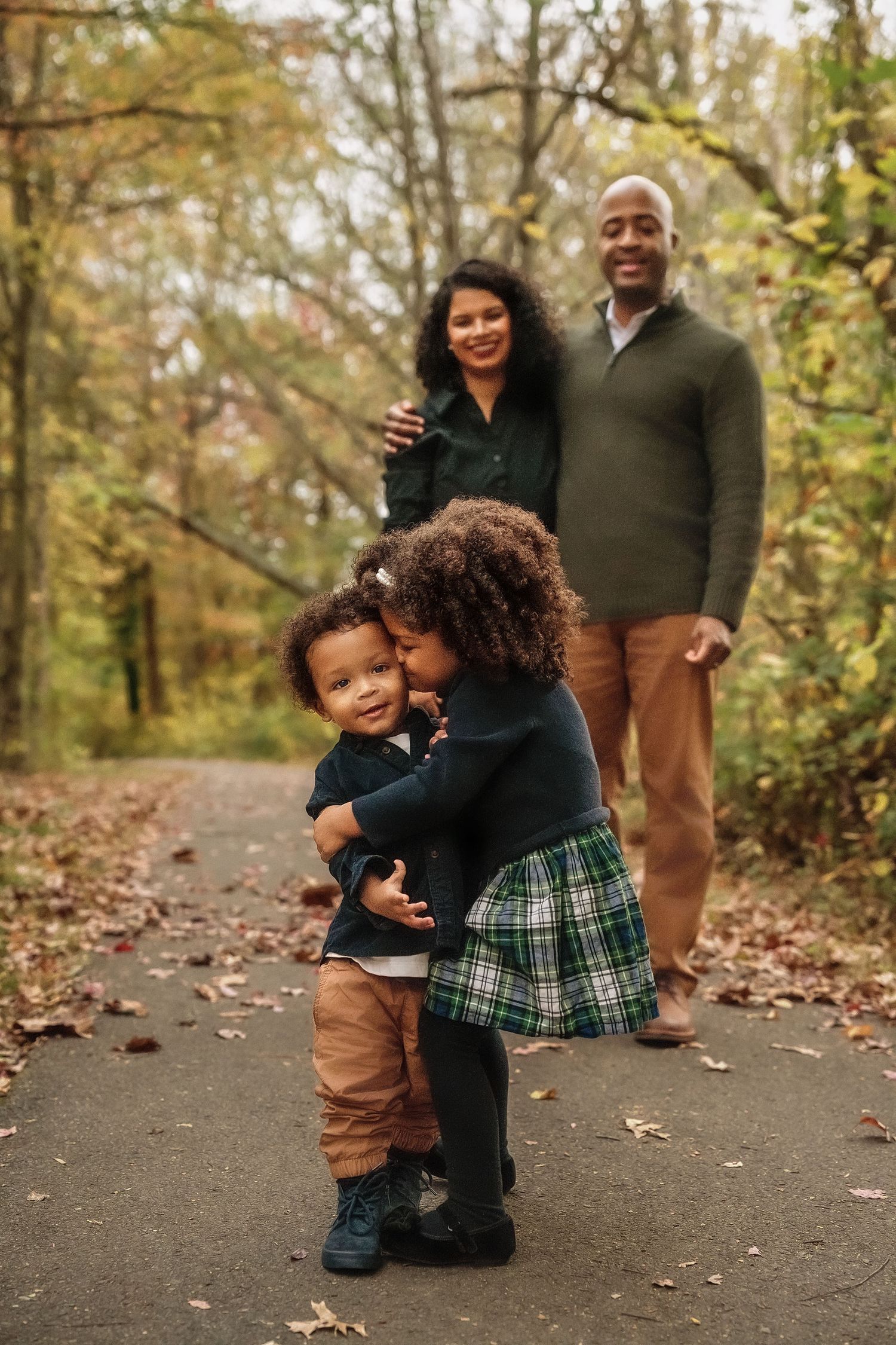 A family shares warm embraces and joyful moments while posing for photos on a leaf-covered forest path in autumn.