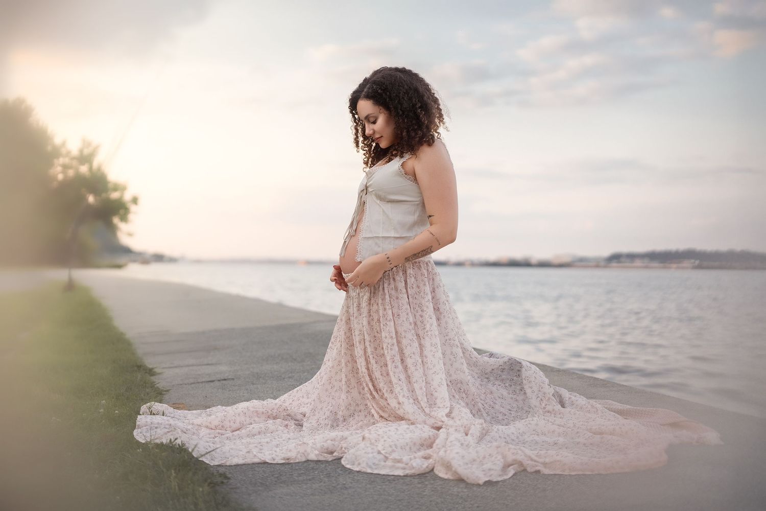 Serene waterfront maternity session with flowing pink dress at sunset.