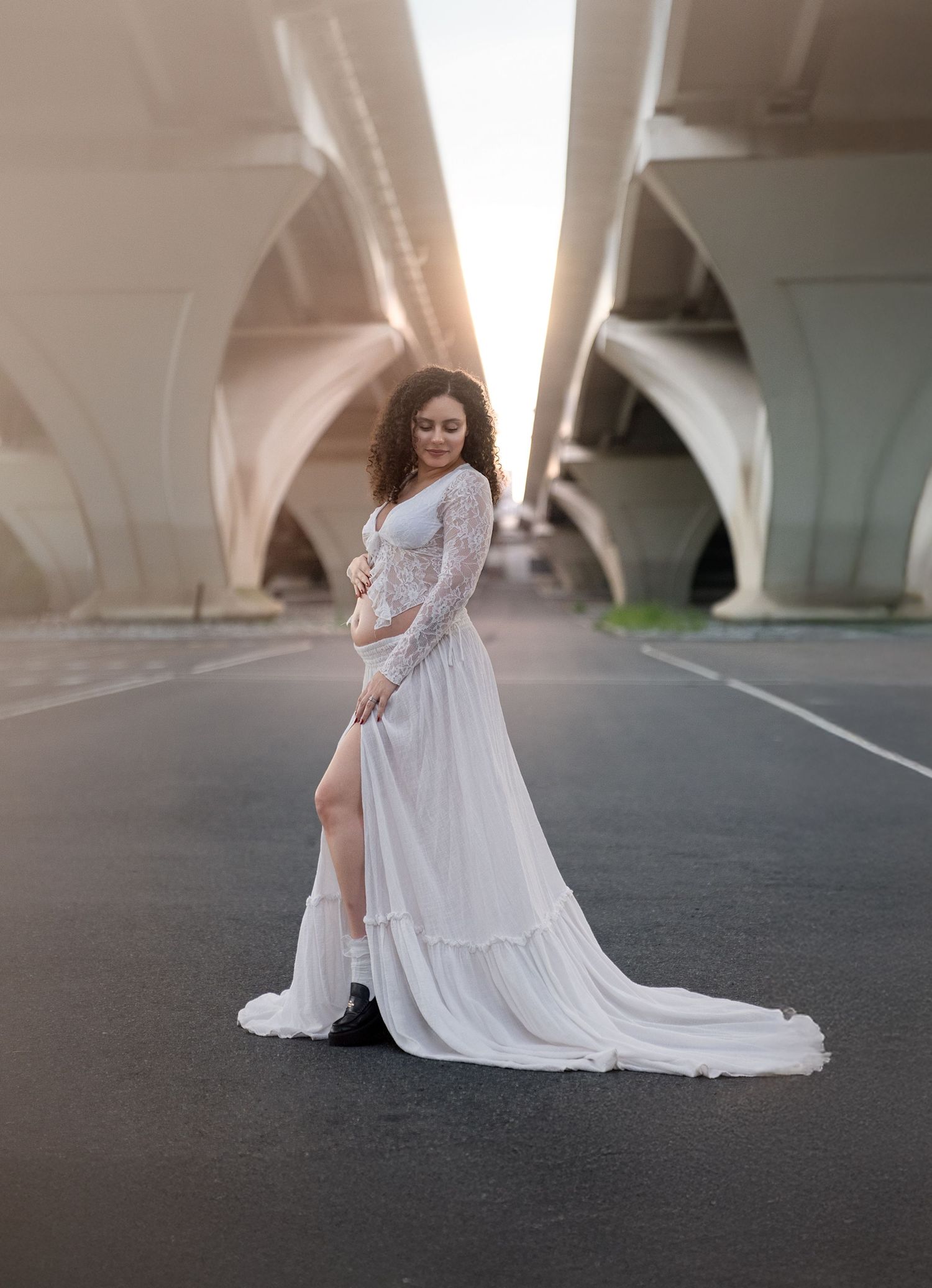 Elegant maternity portraits under bridge featuring flowing white lace gown.