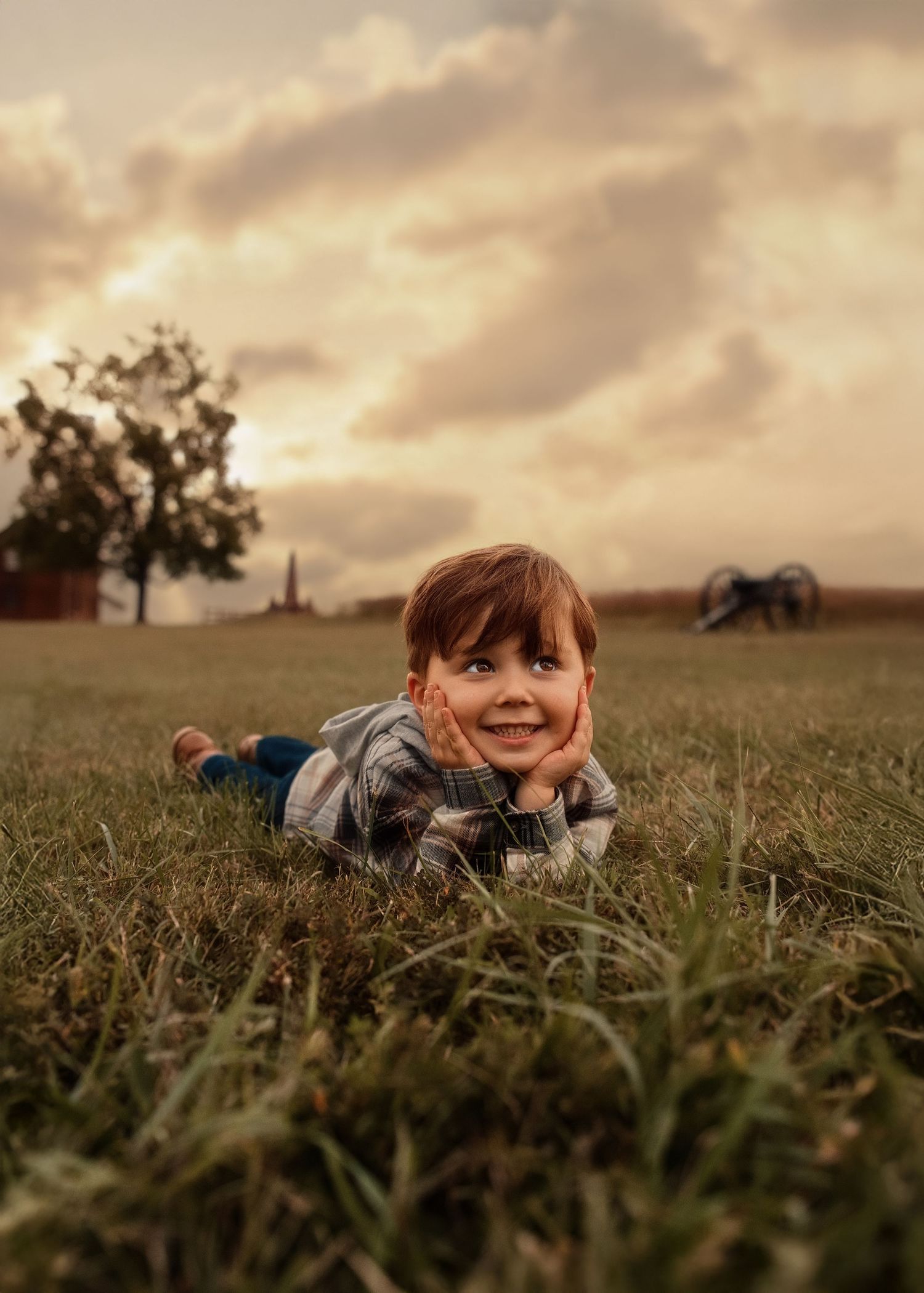 Child lying in tall grass during golden hour with playful expression.