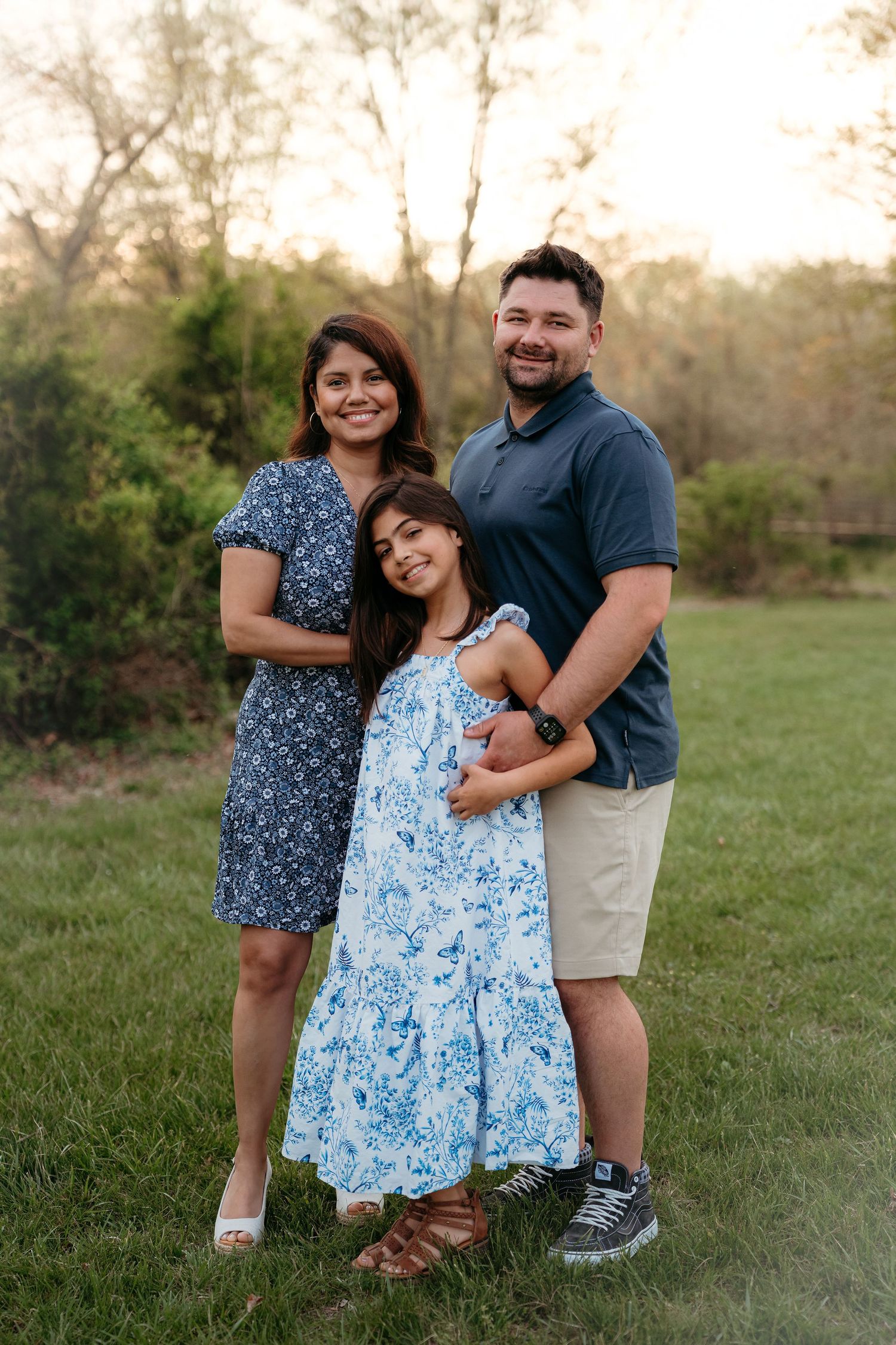 A family wearing blue and khaki outfits poses together outdoors in a grassy field during golden hour in Haymarket Virginia.