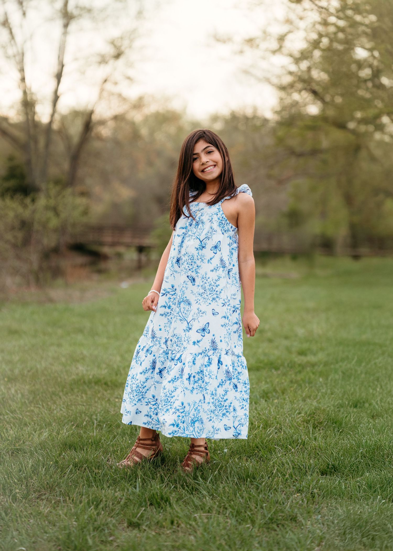 A sleeveless blue and white floral maxi dress paired with brown sandals on green grass.