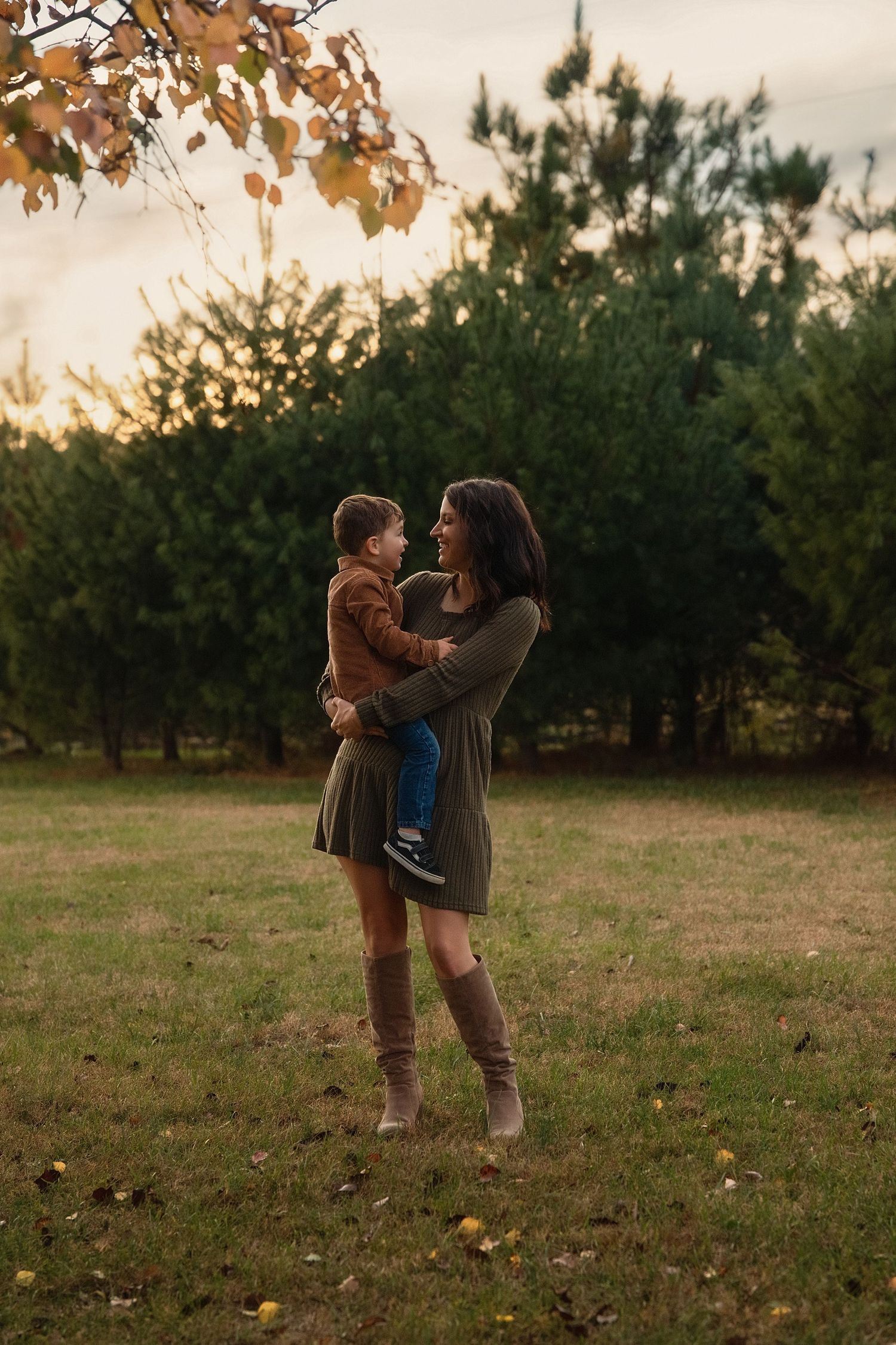 Parent and child play together in an autumn field at sunset with fallen leaves scattered on the ground.