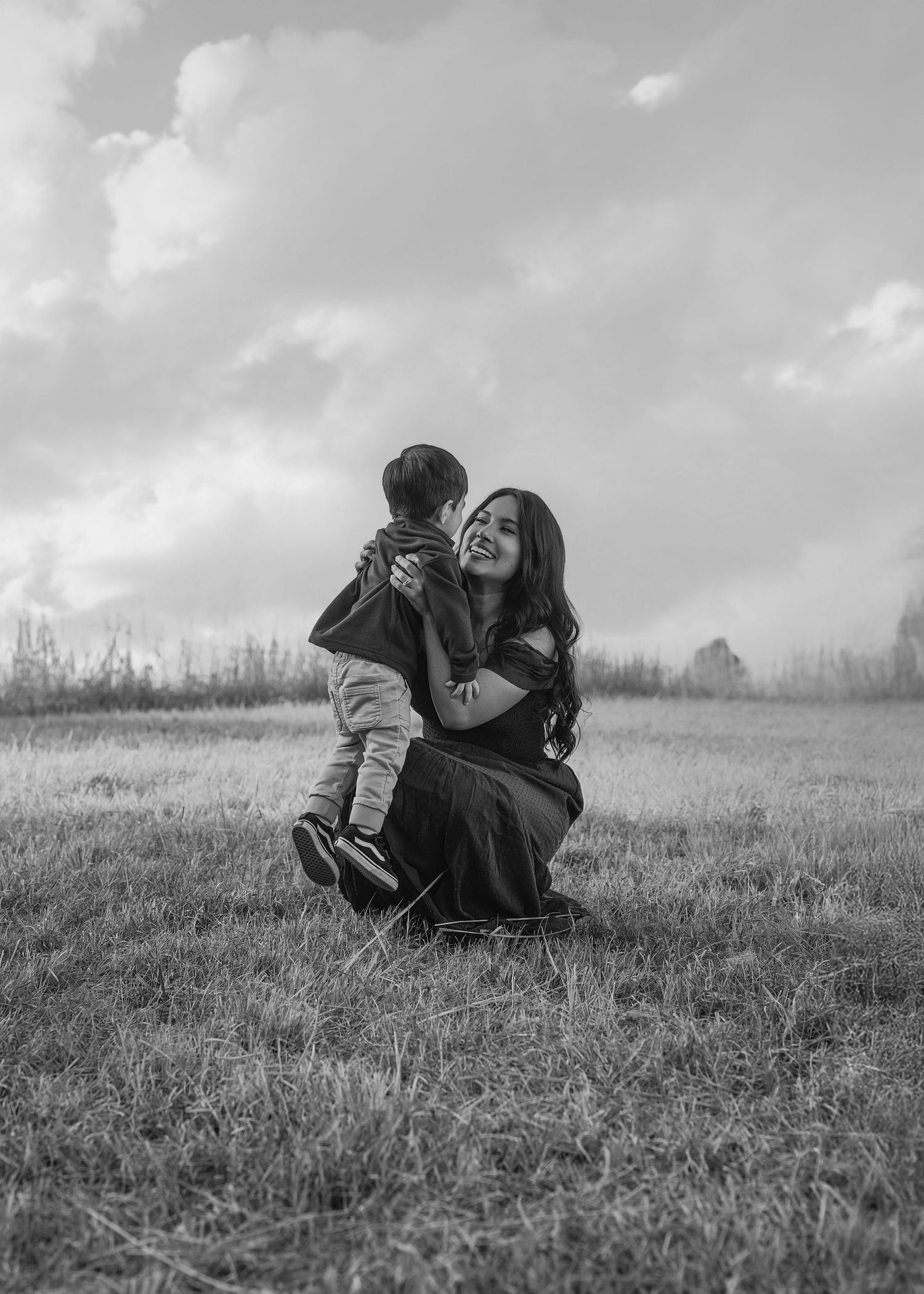 A black and white photo series shows two people lying together on a grassy hillside under cloudy skies.