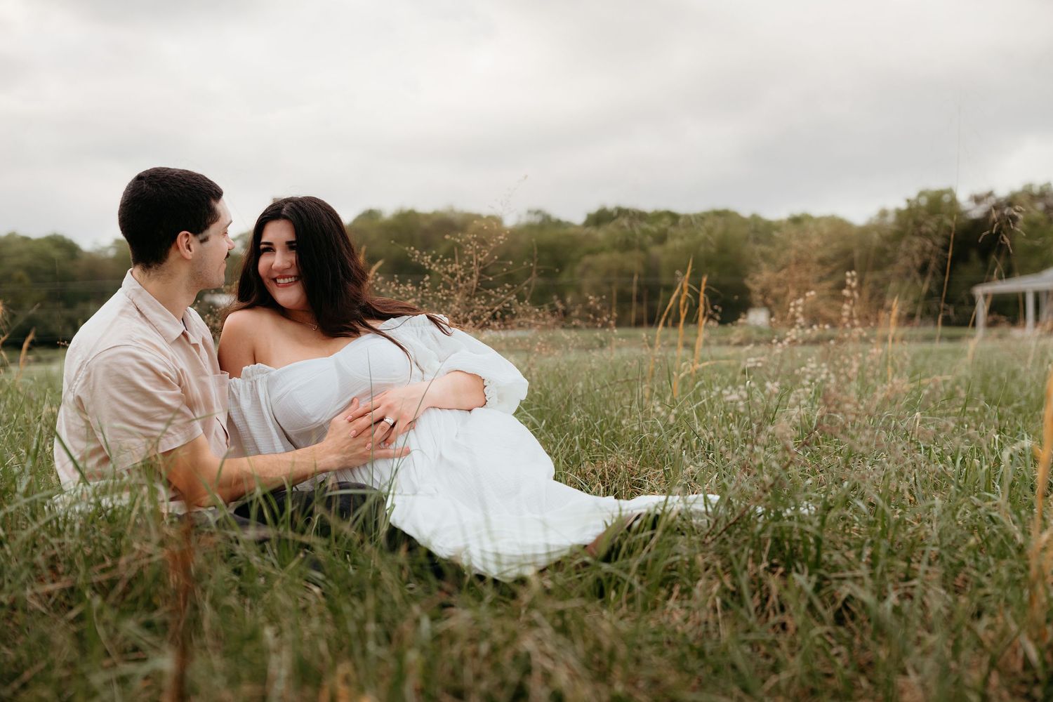 Romantic couple laying in tall grass during sunset photoshoot in countryside.