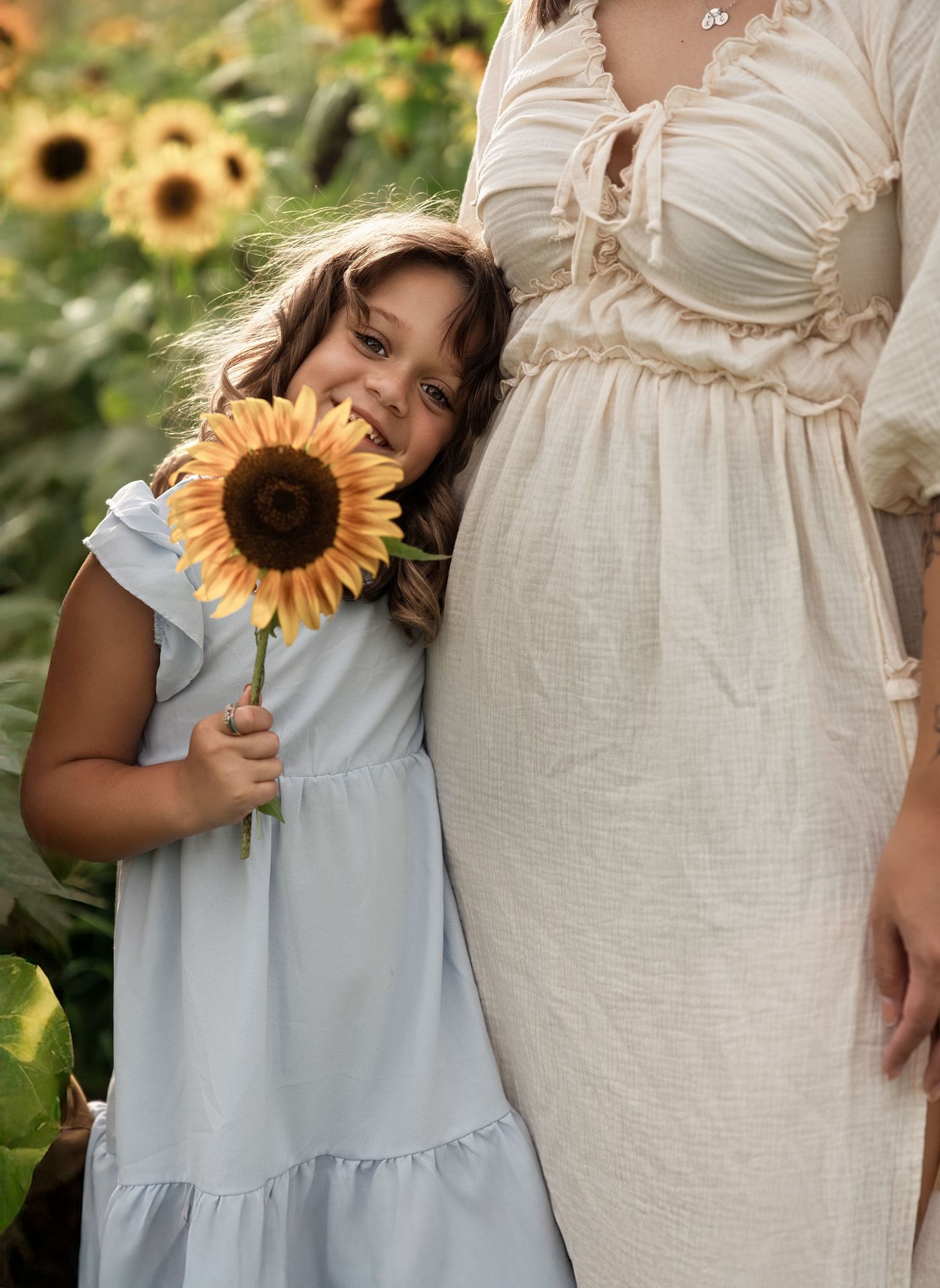 Children in light blue dresses holding sunflowers next to woman in white dress.