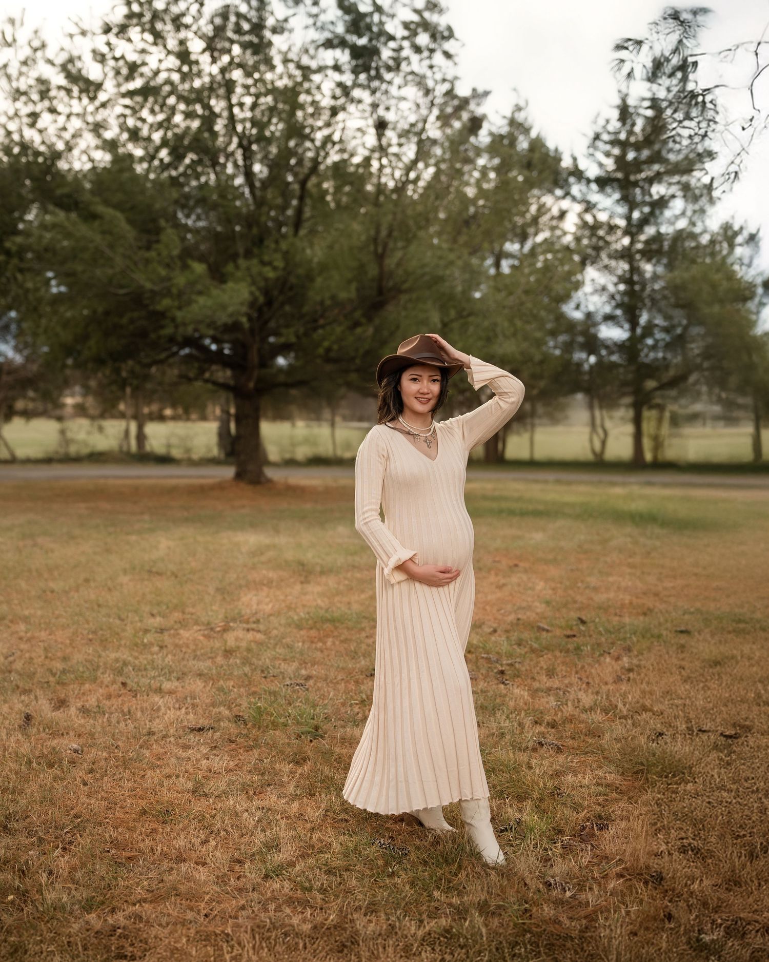 Woman in flowing pink dress twirls and poses in a rustic field during golden hour.