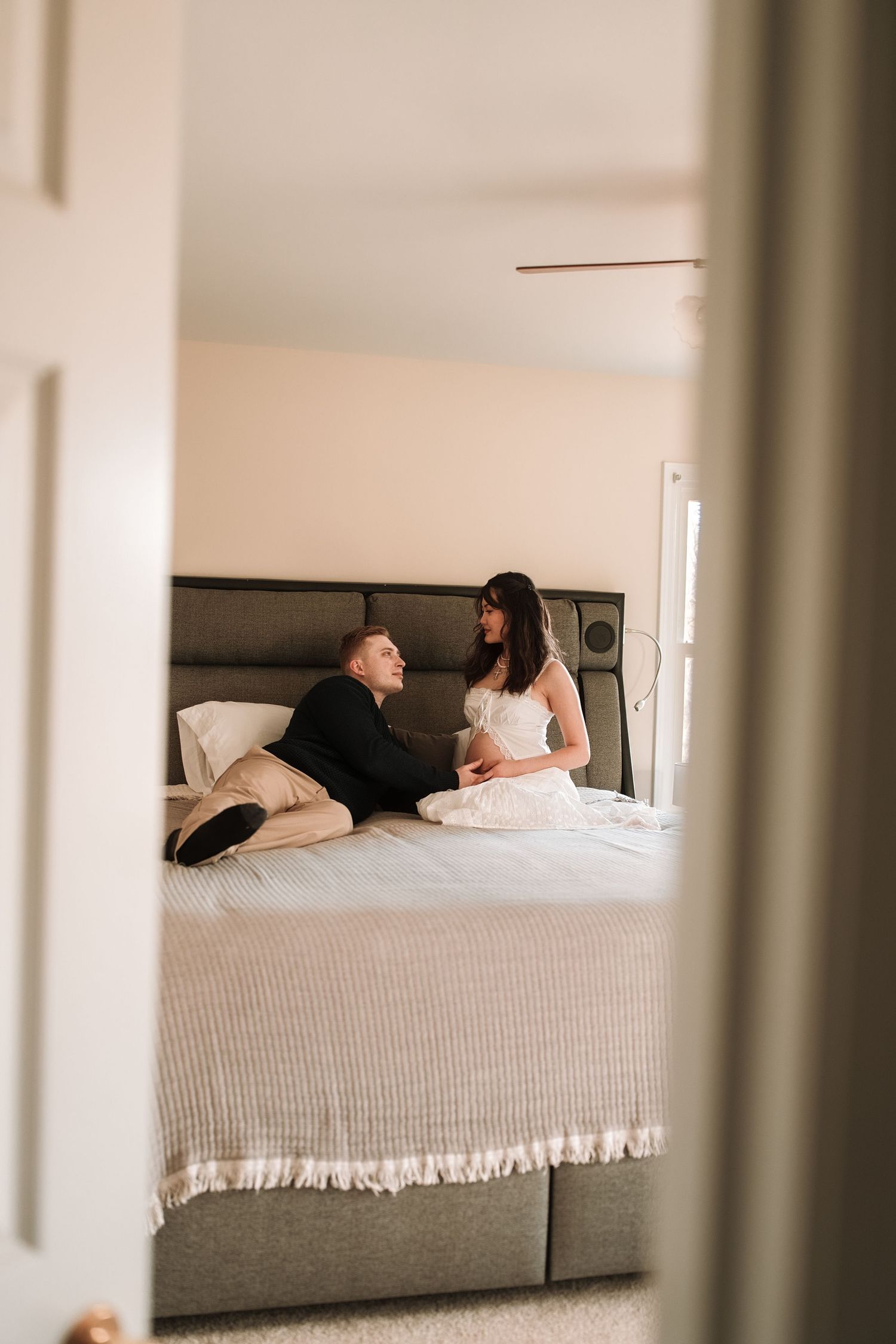 Artistic maternity boudoir photos captured on a bed with soft natural lighting through window frames.