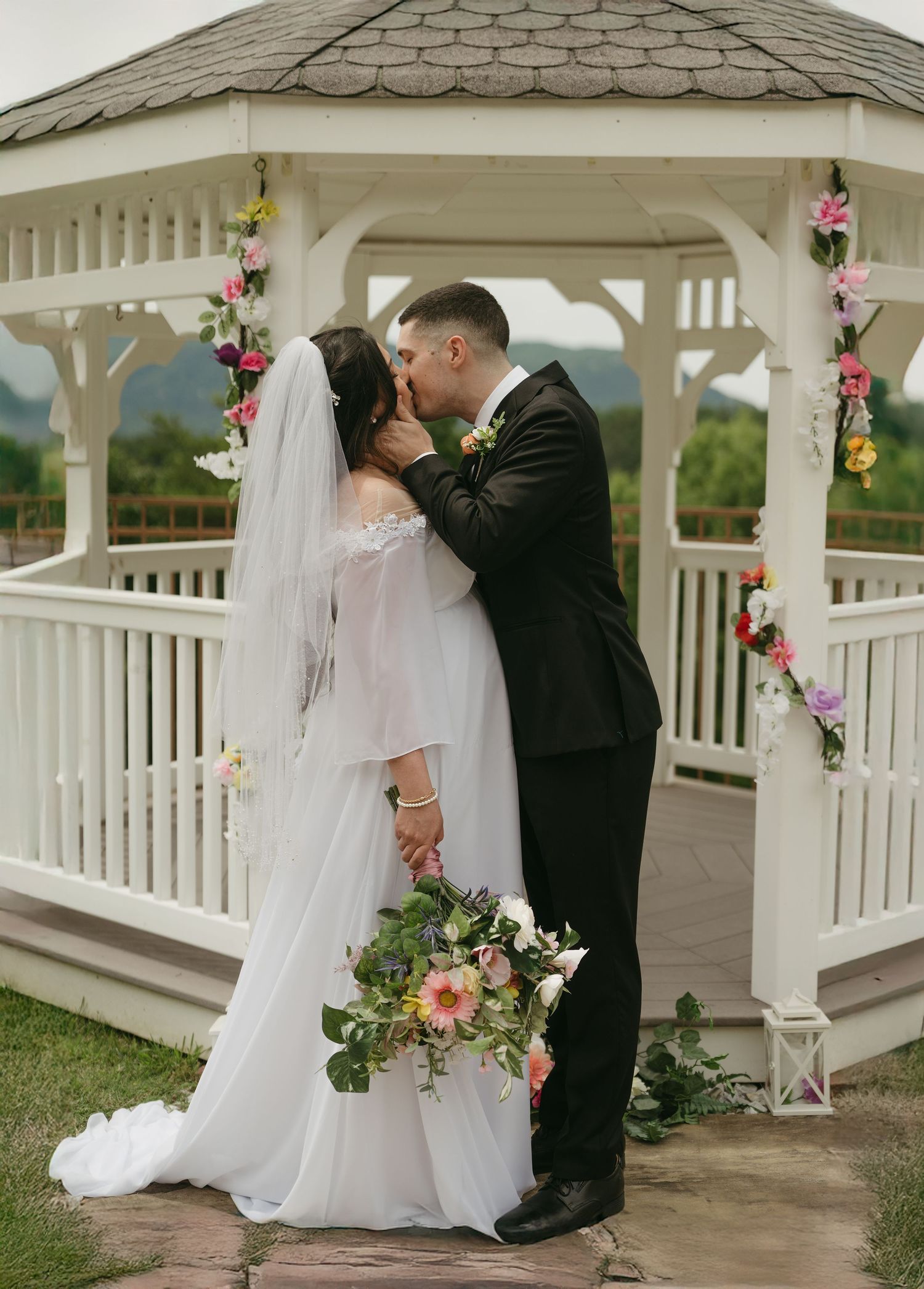 Wedding couple shares intimate moment under white gazebo decorated with pink and purple flowers.