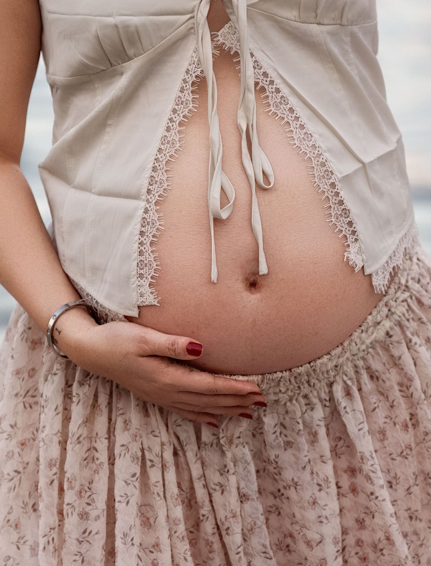 Close-up details of lace maternity dress and baby bump in soft lighting.