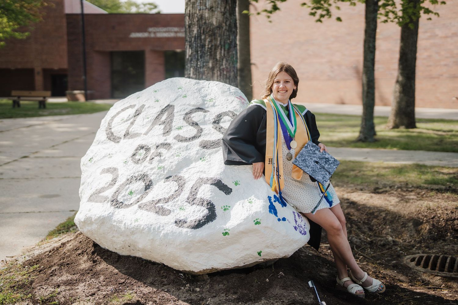 Students gather around a large painted rock on a college campus during a sunny day.