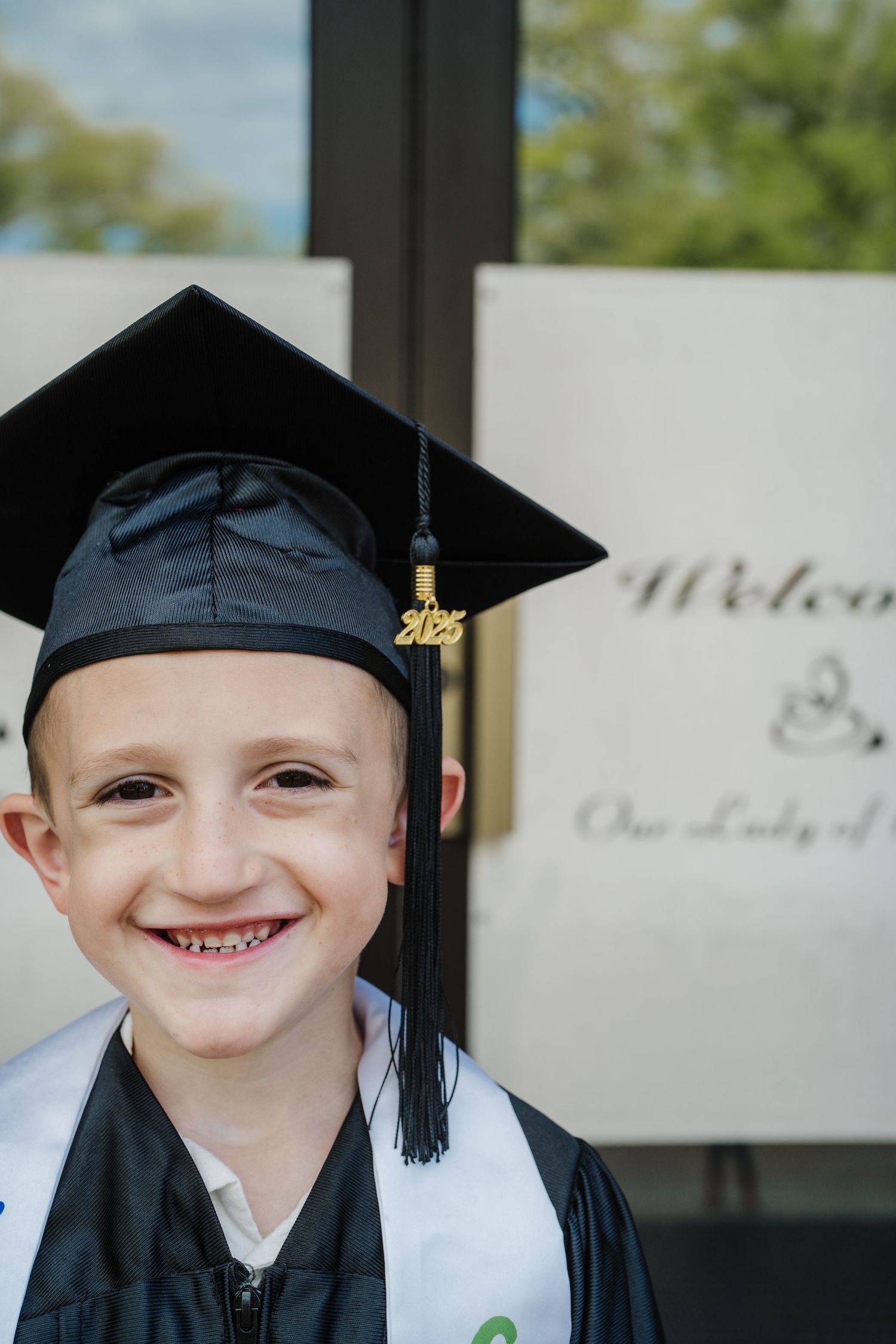 Graduate in black cap and gown smiling against a light background.