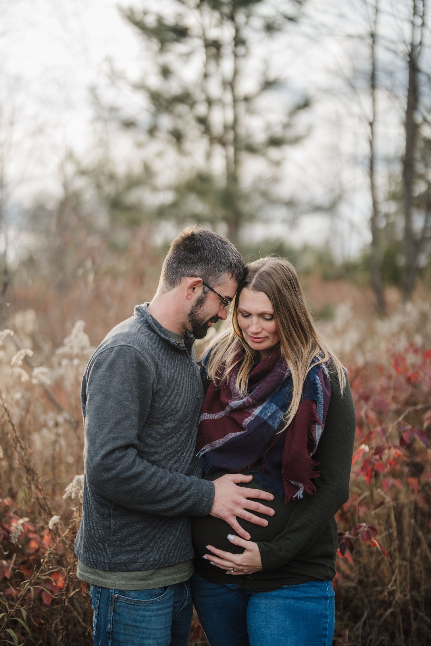A couple shares intimate moments together in a field with autumn foliage and tall grass in the background.