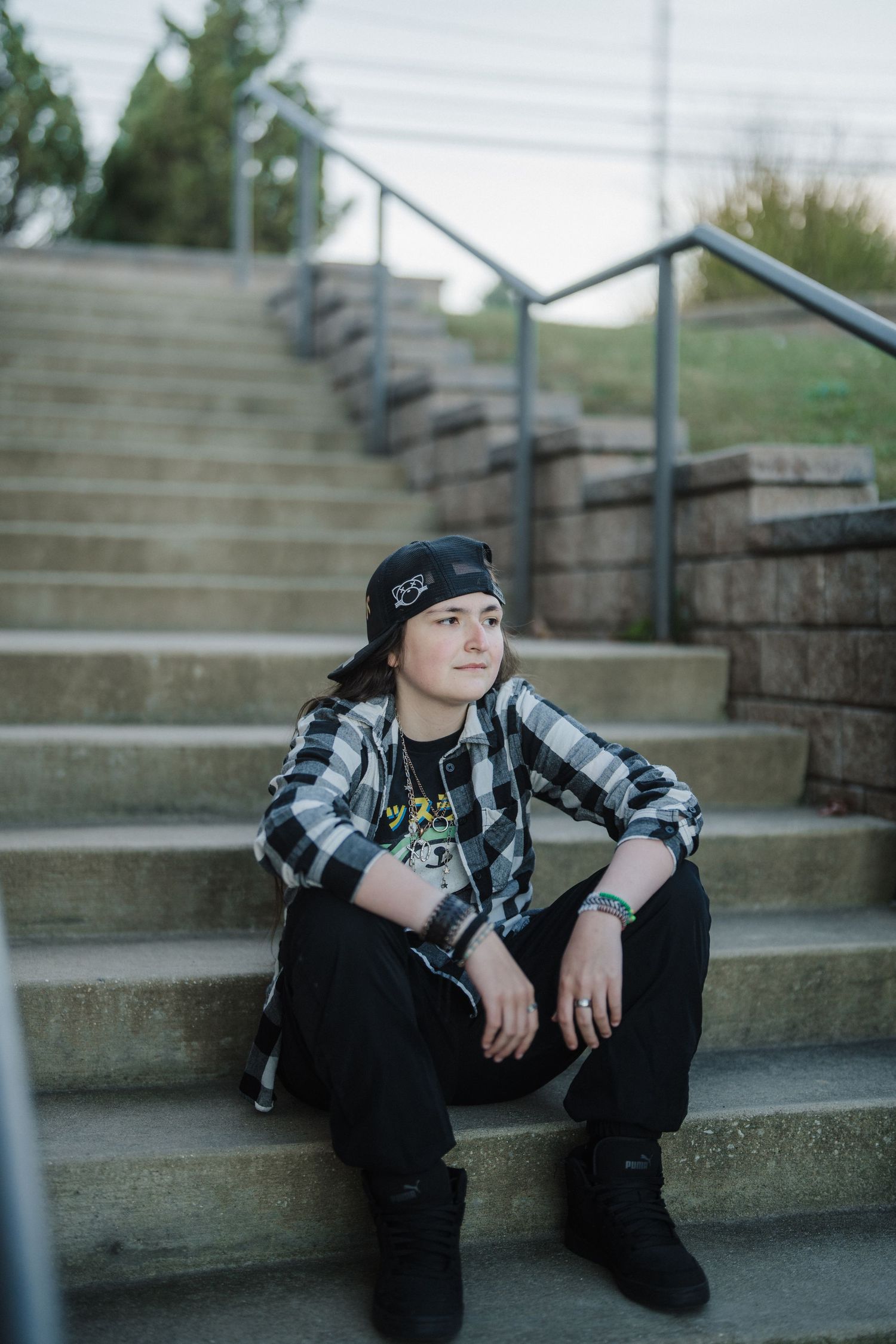 A person wearing a plaid shirt and beanie sits thoughtfully on concrete steps in a moody outdoor setting.