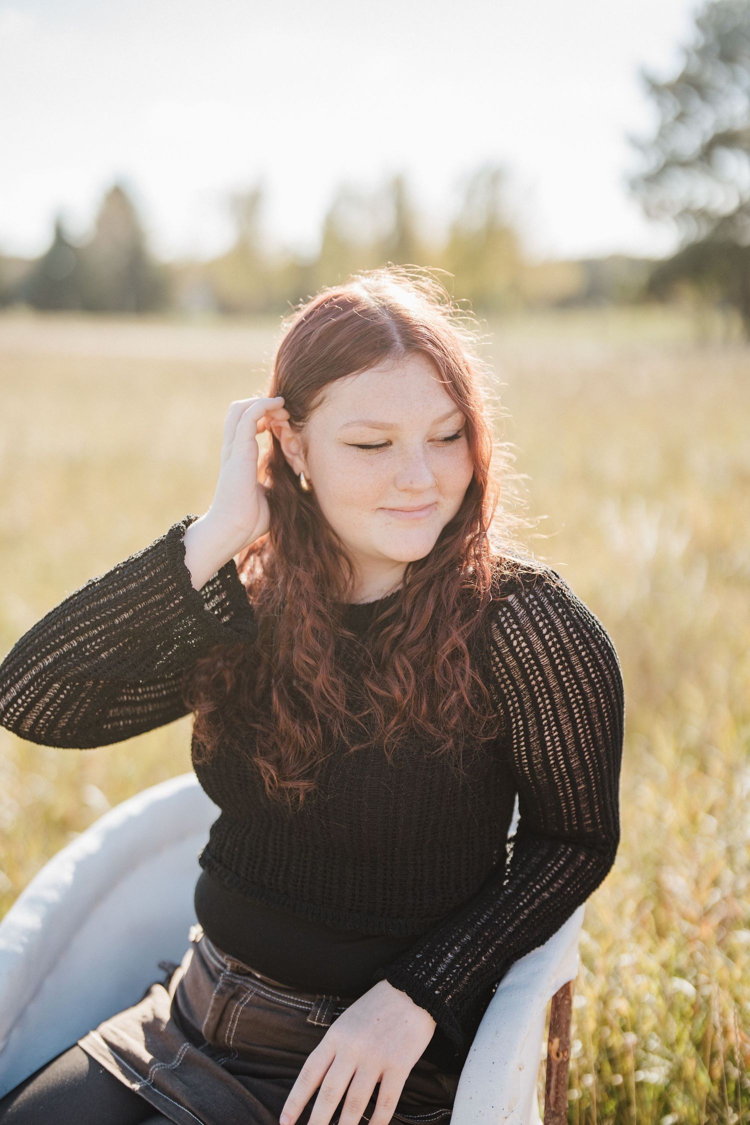 Person in black sweater sitting in sunny field with wildflowers during golden hour.