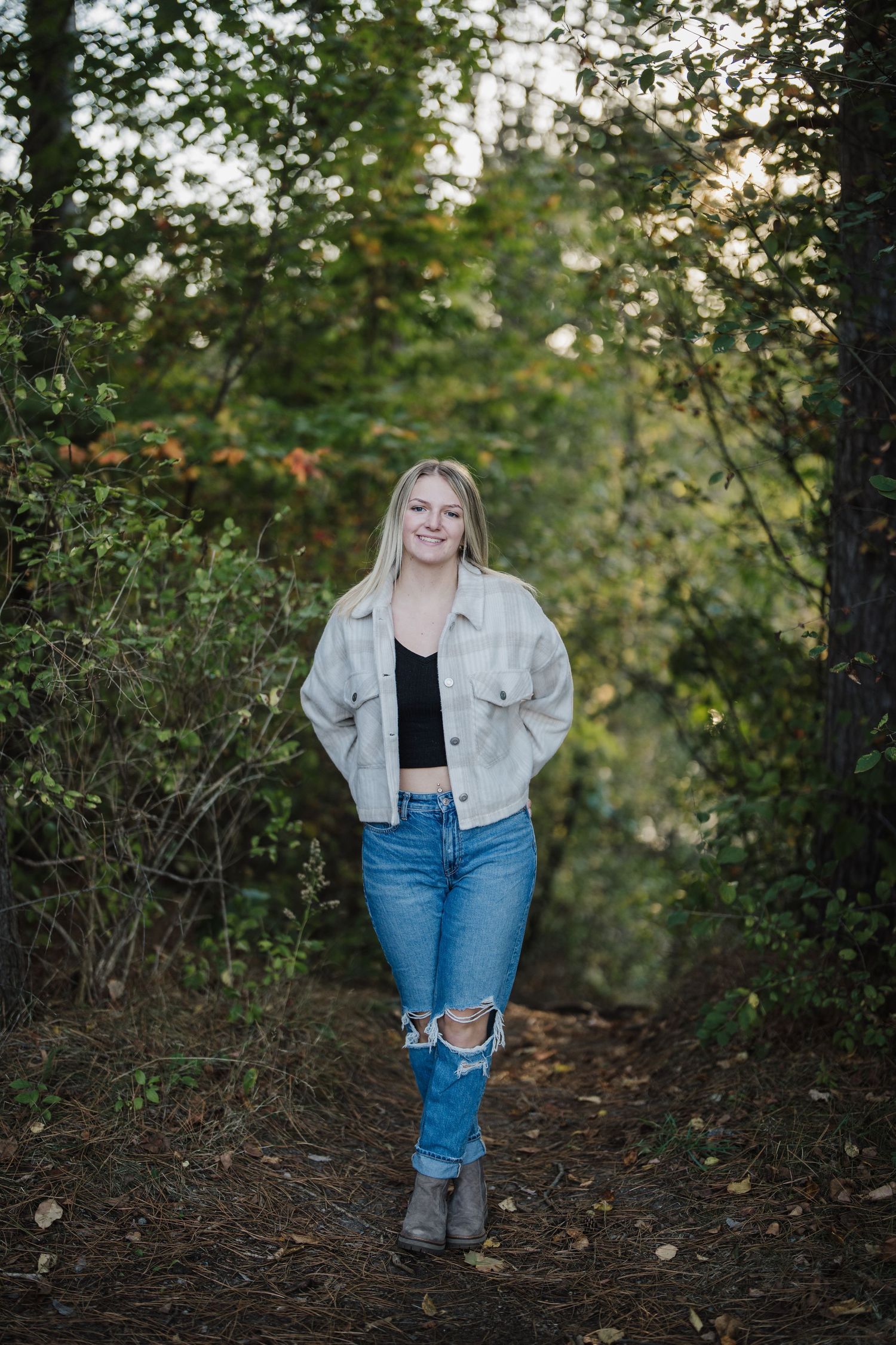 A casual outdoor photoshoot in a wooded area with fallen leaves and natural lighting.