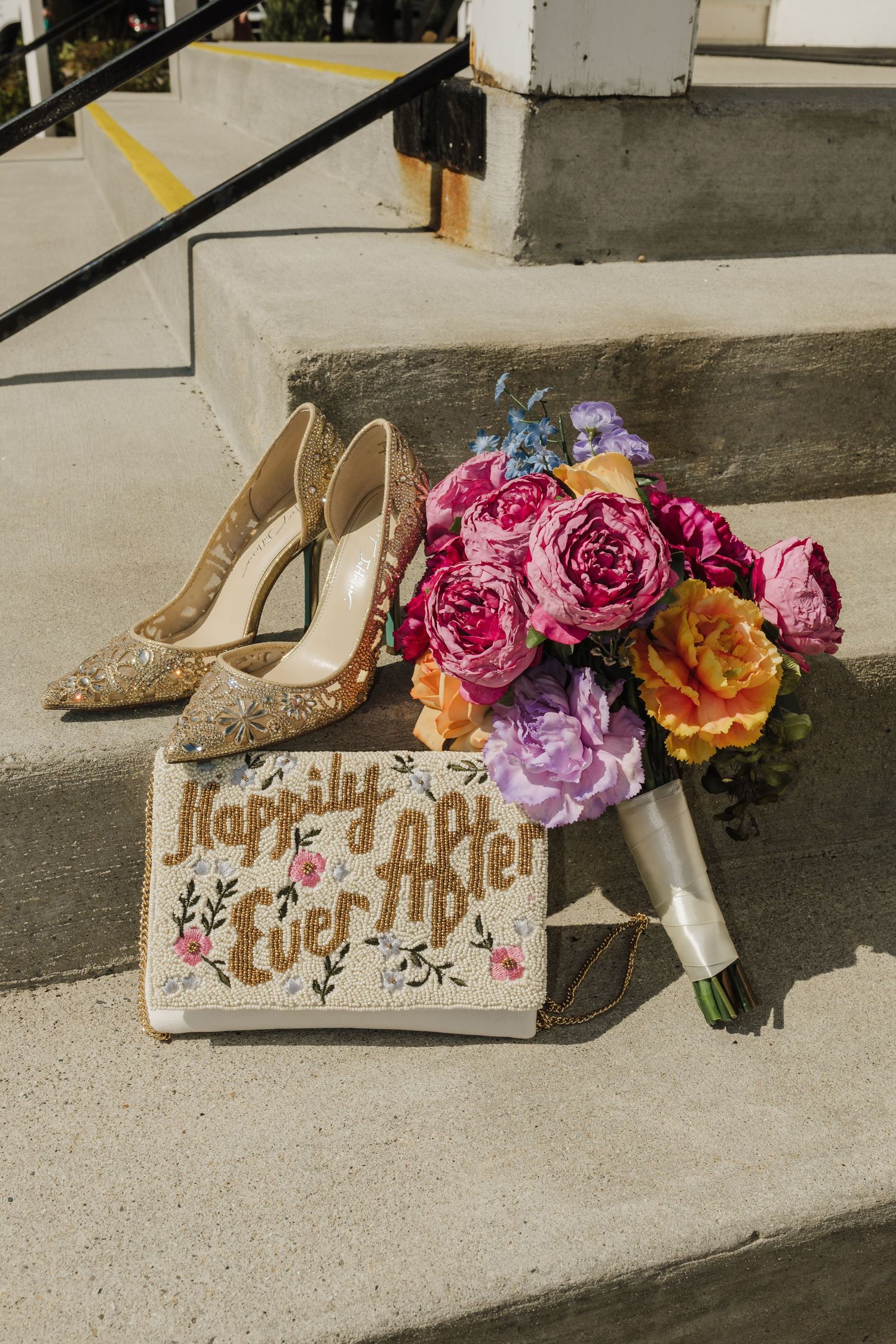 Wedding shoes and colorful floral arrangements arranged on concrete steps with text decorations.