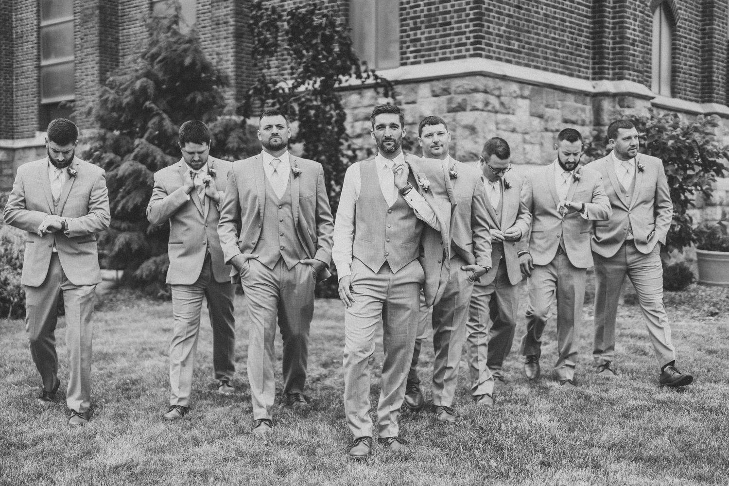 Black and white photo of groomsmen walking in unison across a lawn.