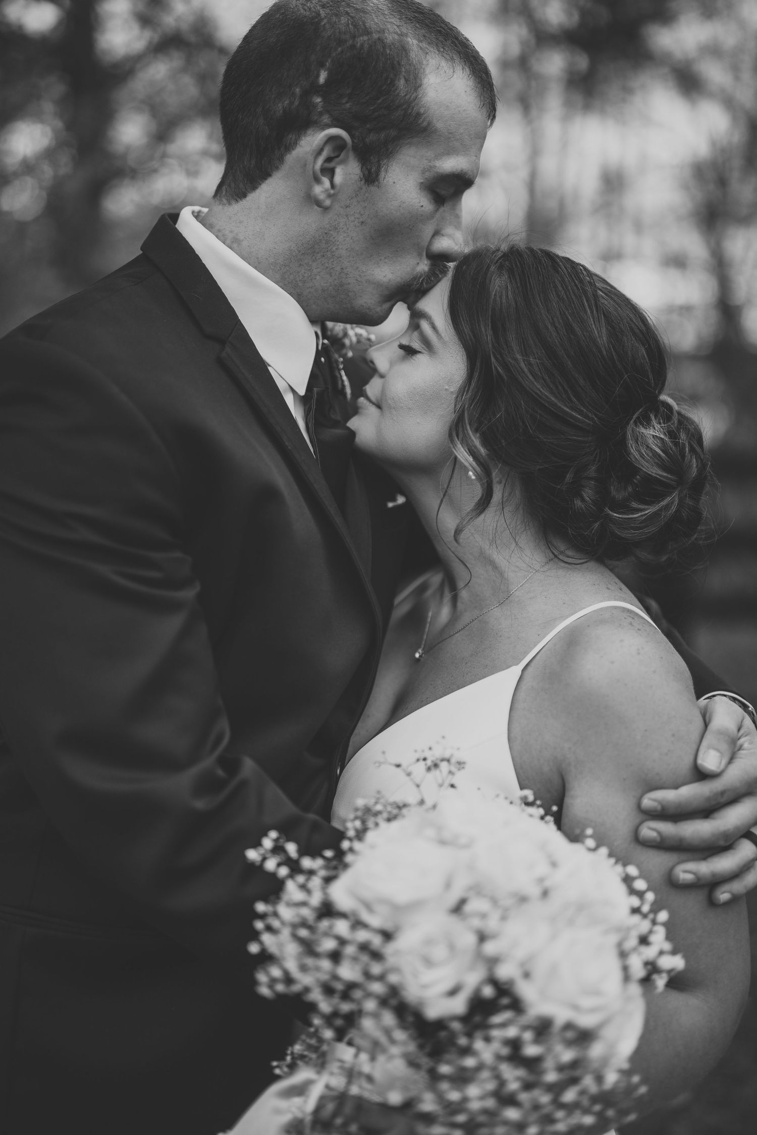 A romantic black and white wedding photo showing a tender moment between newlyweds with baby's breath bouquet.