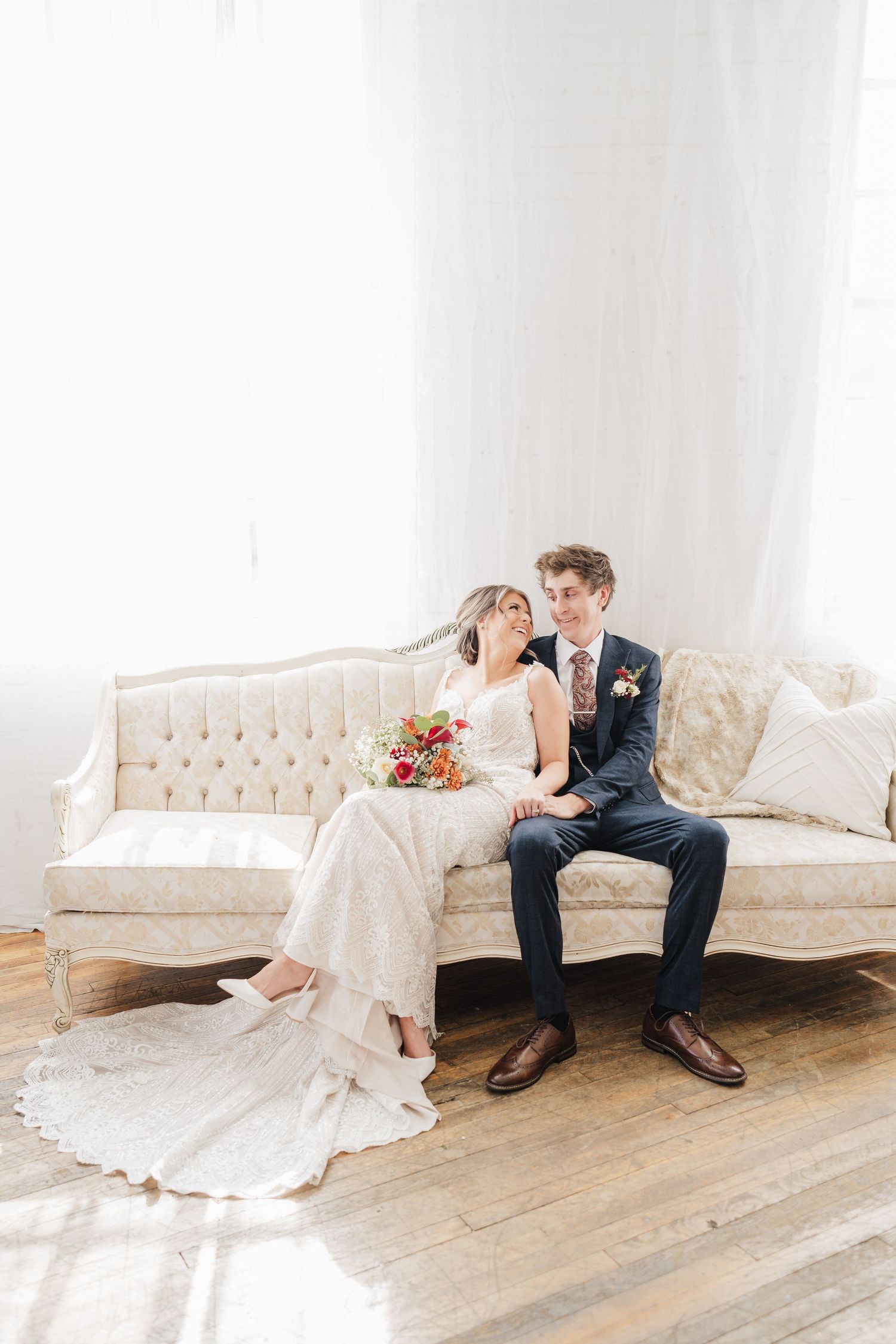 Elegant wedding portrait on vintage white tufted sofa in bright minimalist room.