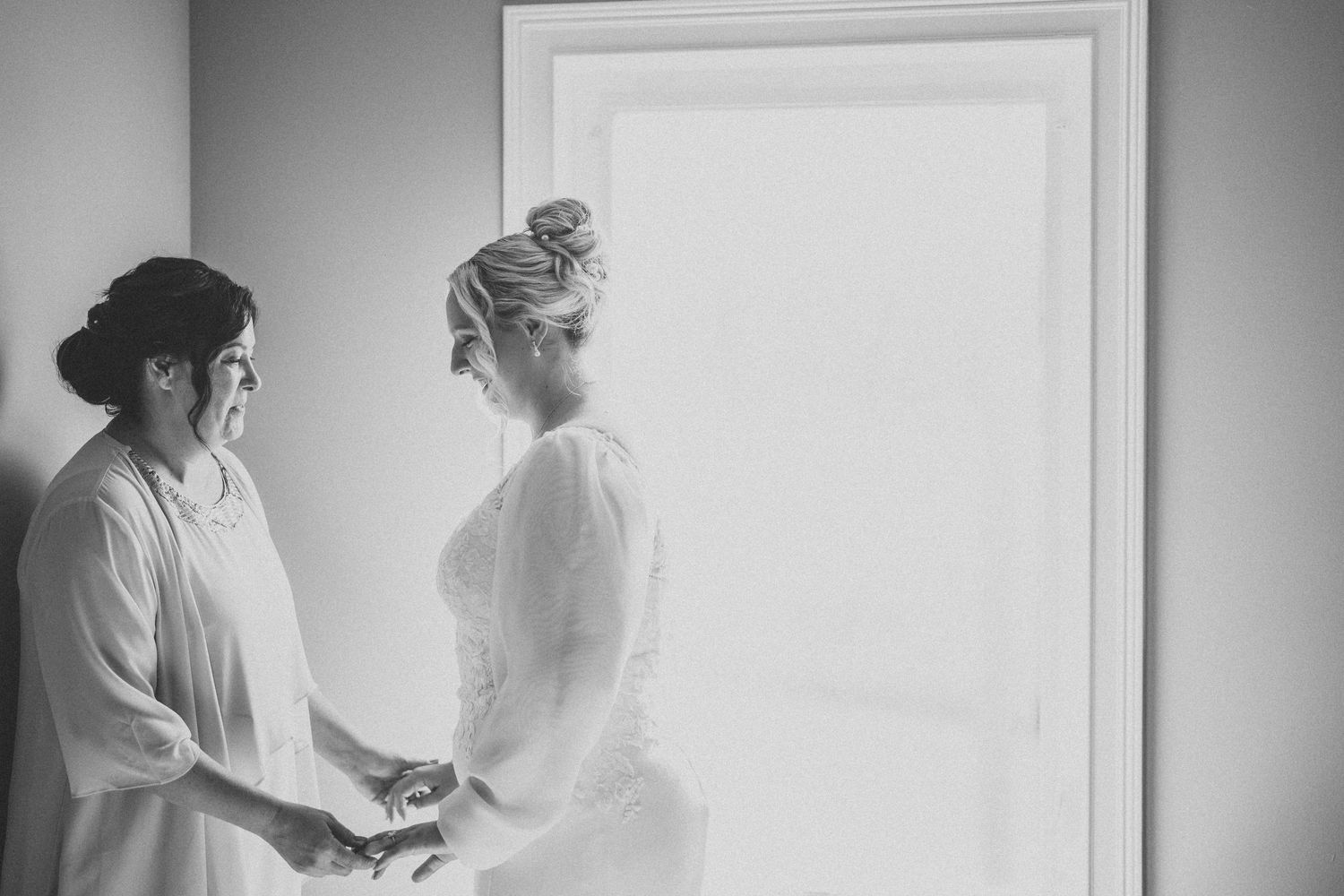 Two women share an intimate black and white moment before a wedding ceremony.