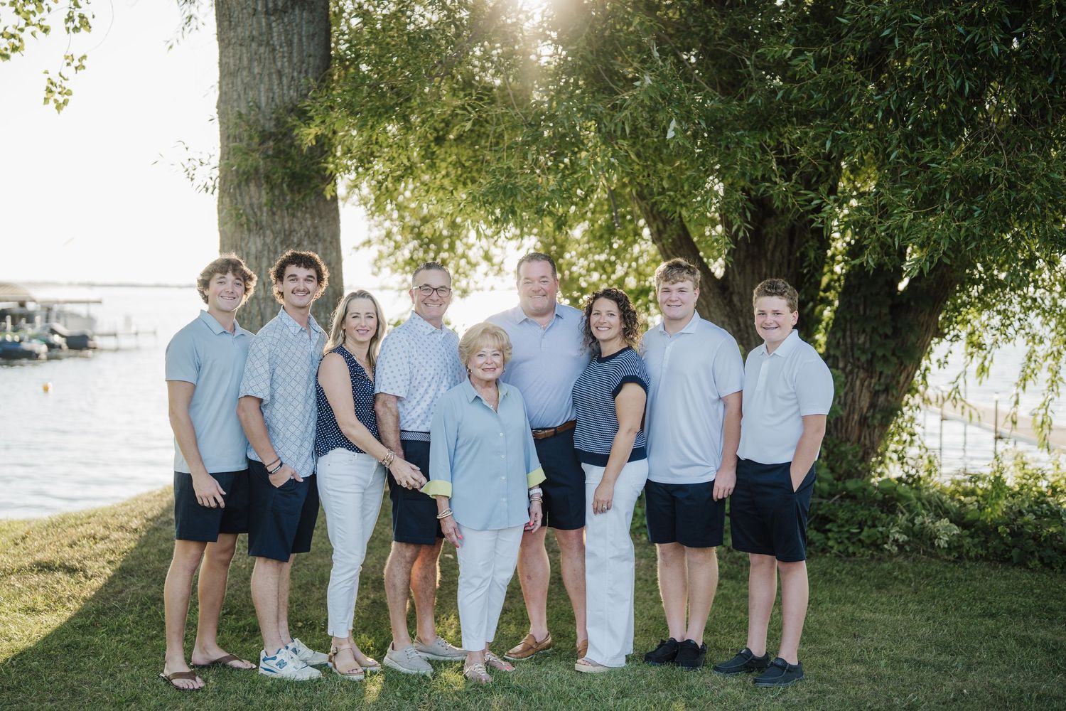 Family group poses together outdoors near water during golden hour with trees in background.