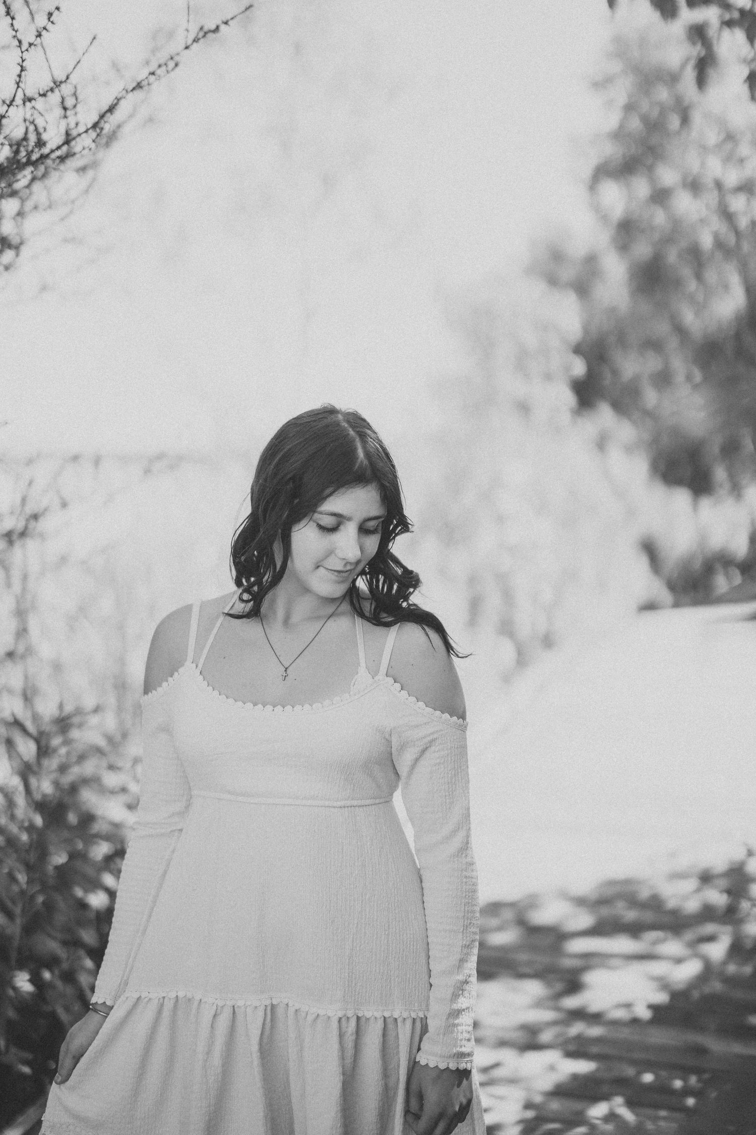 A black and white portrait showing someone in a white dress looking down thoughtfully.