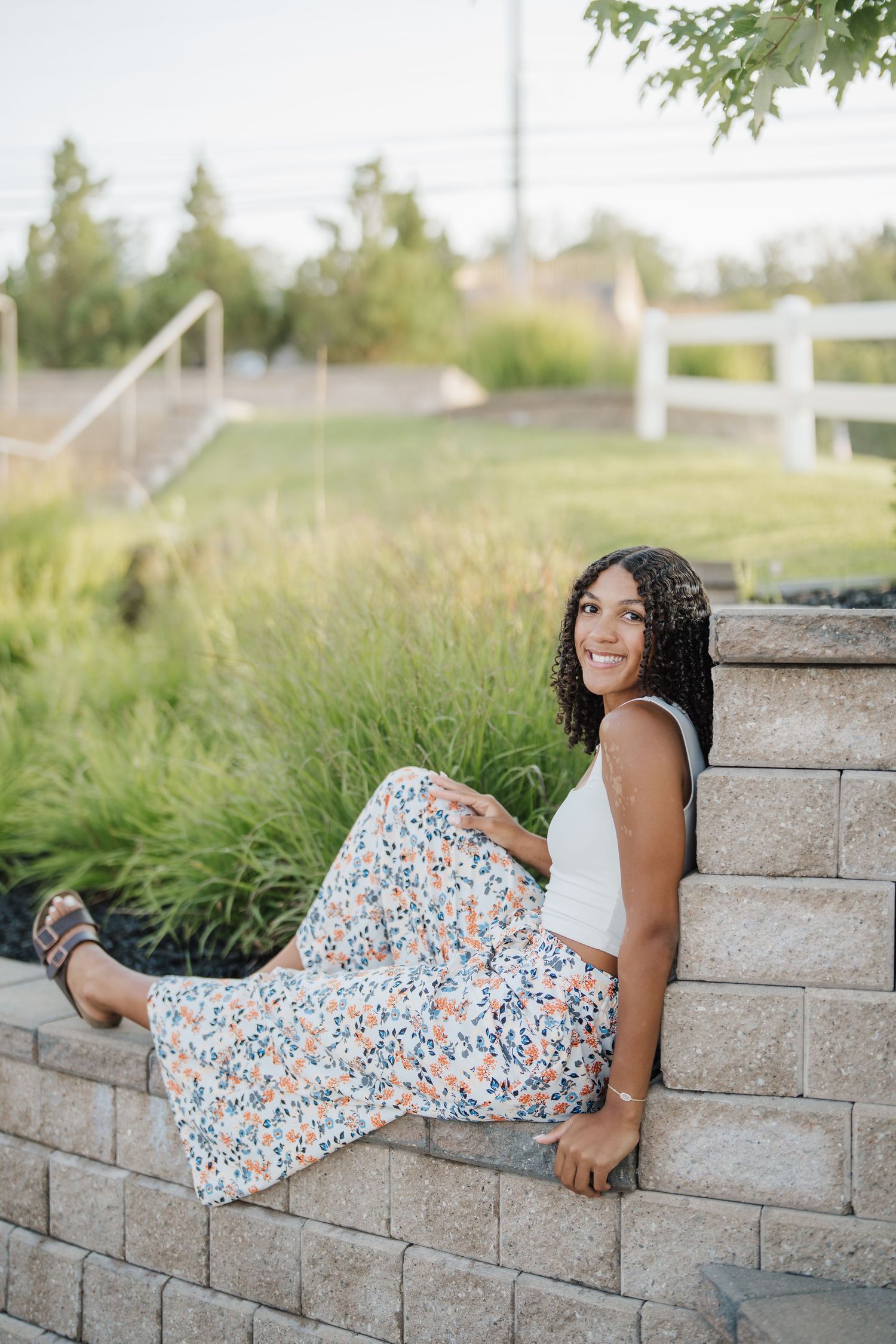 A floral dress photoshoot on stone retaining wall blocks in an outdoor garden setting.