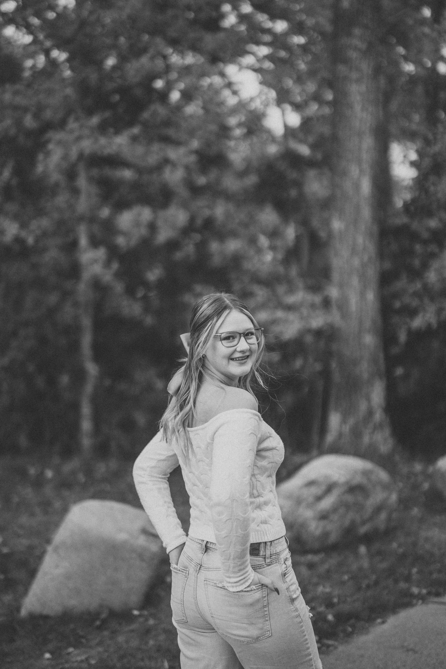 Black and white series of photos showing a young child in a white dress playing and twirling outdoors in a wooded setting.