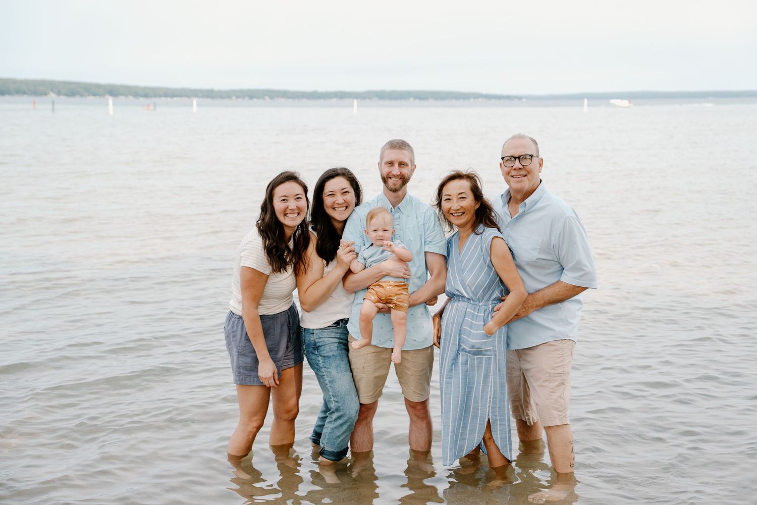 Multi-generational family smiling together while standing in shallow lake water during a outdoor photo session.