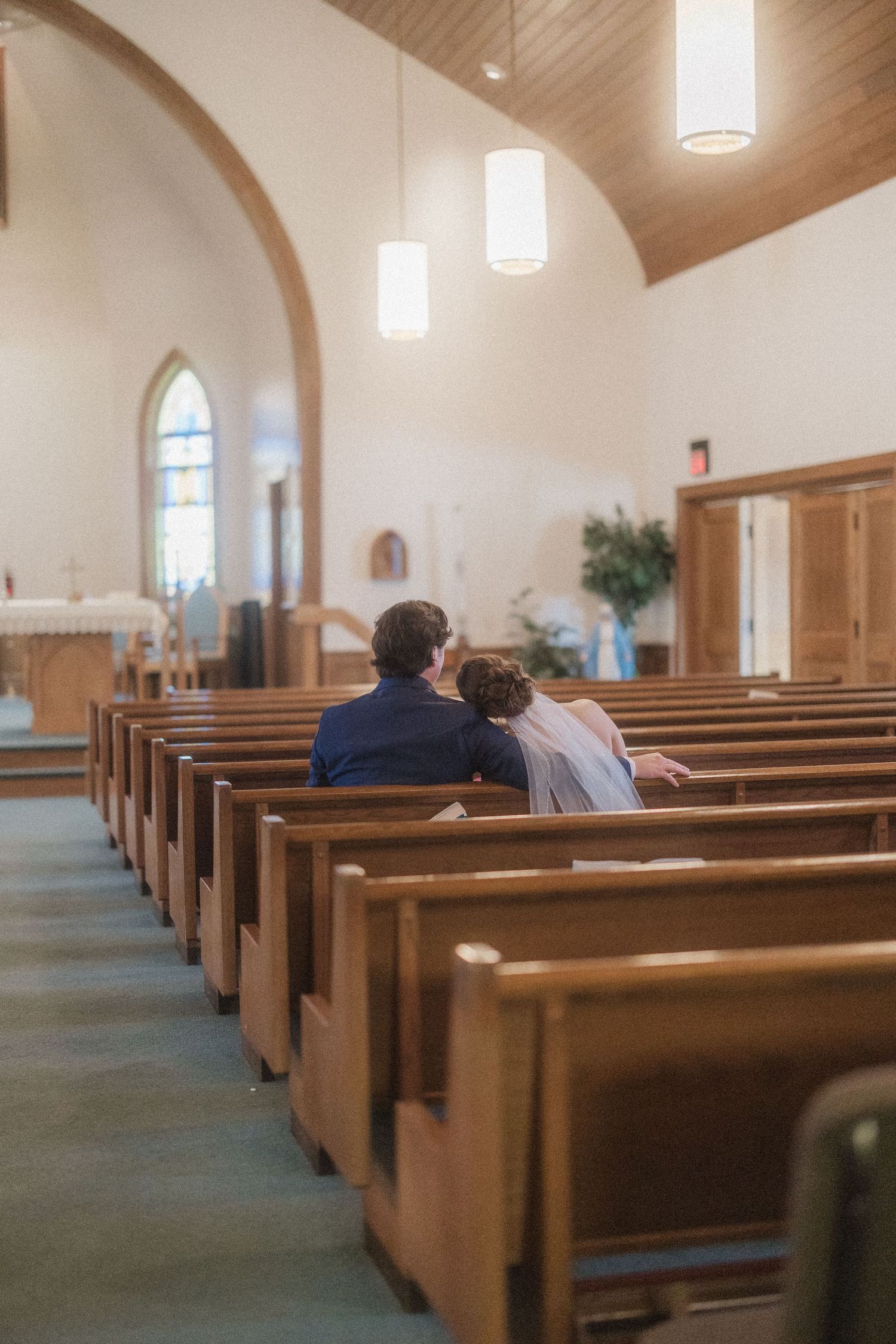 Empty wooden church pews in a sunlit sanctuary with vaulted ceilings and stained glass windows.