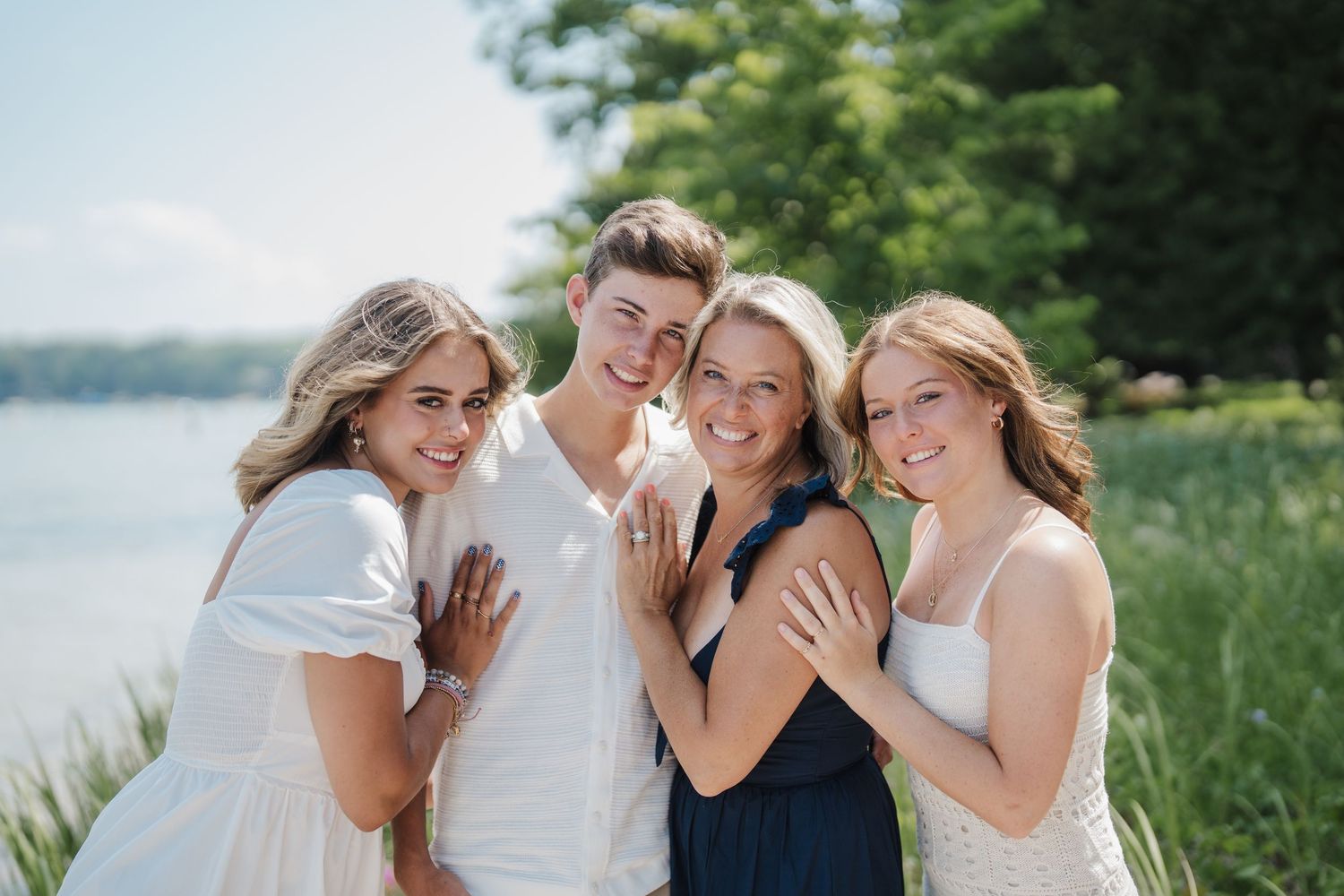 Group of people in white clothing laughing and embracing on a sunny beach during a casual outdoor photoshoot.