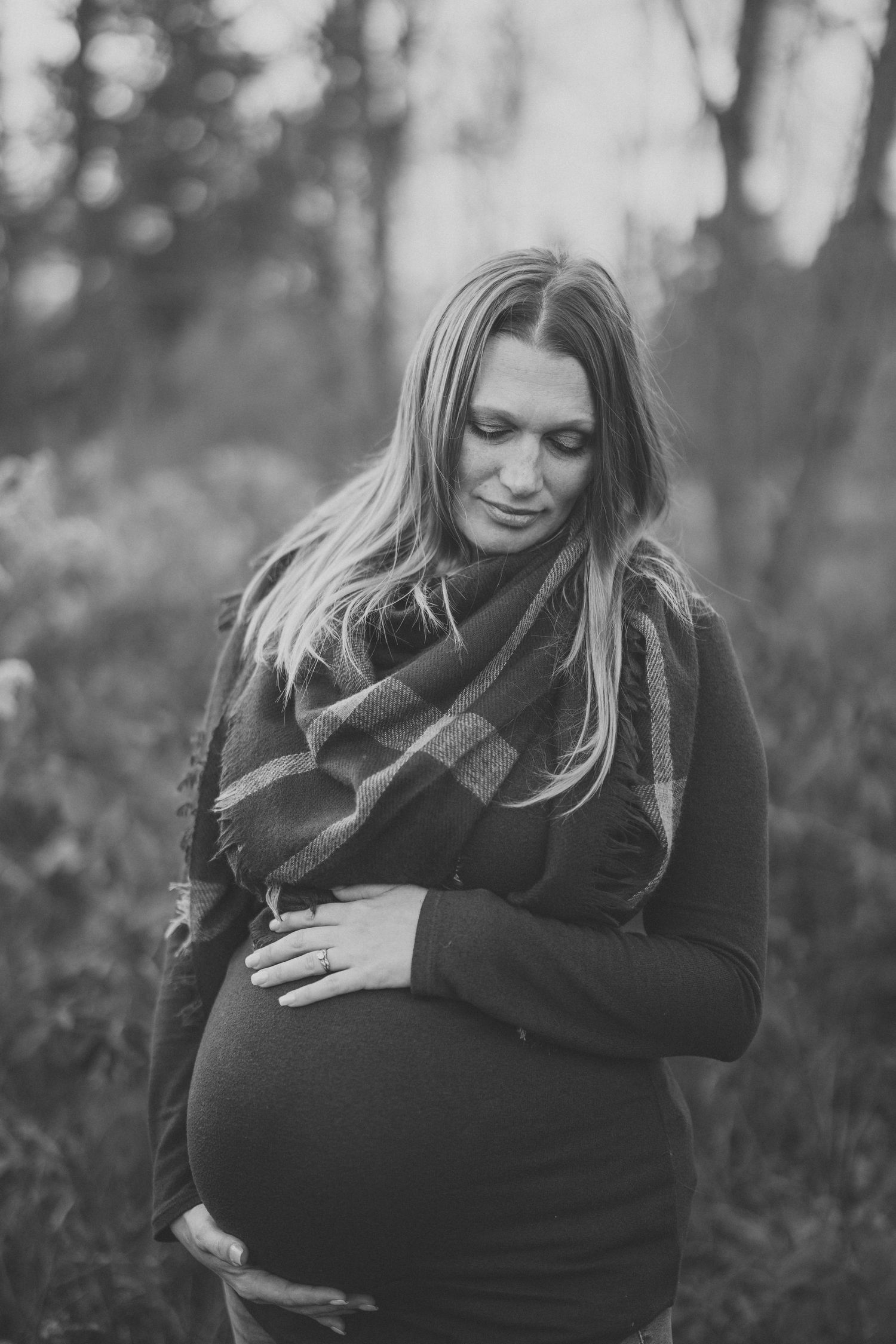 A series of black and white maternity photos showing a pregnant woman in a black sweater embracing her belly outdoors.