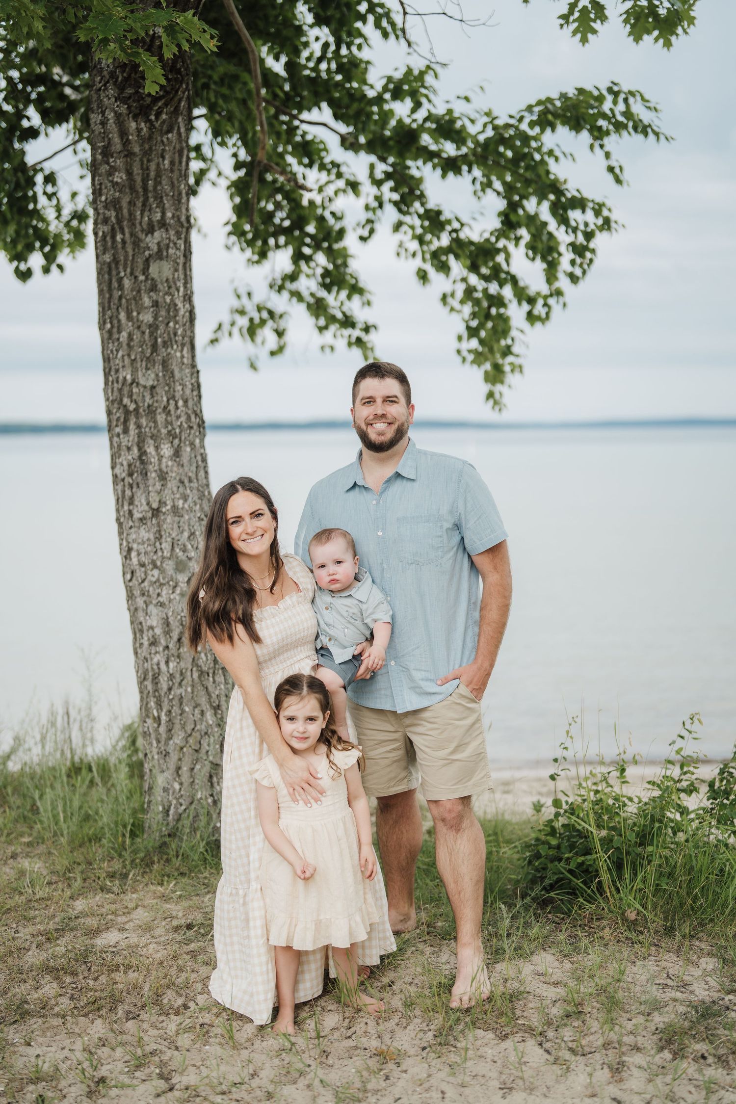 A family poses together on a beach with trees and water in the background.
