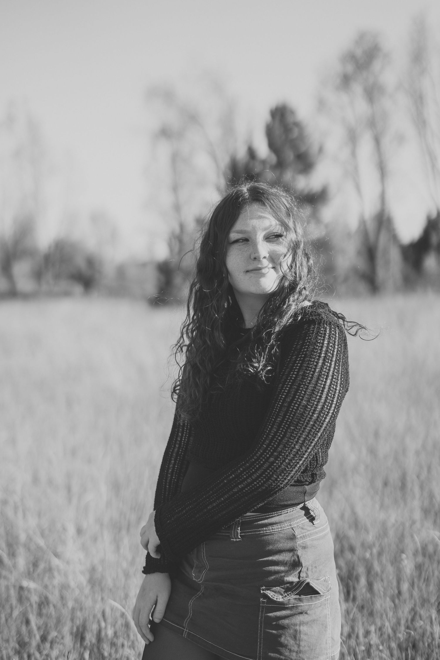A black and white photo series showing a woman wrapped in a knit scarf standing in a grassy field.