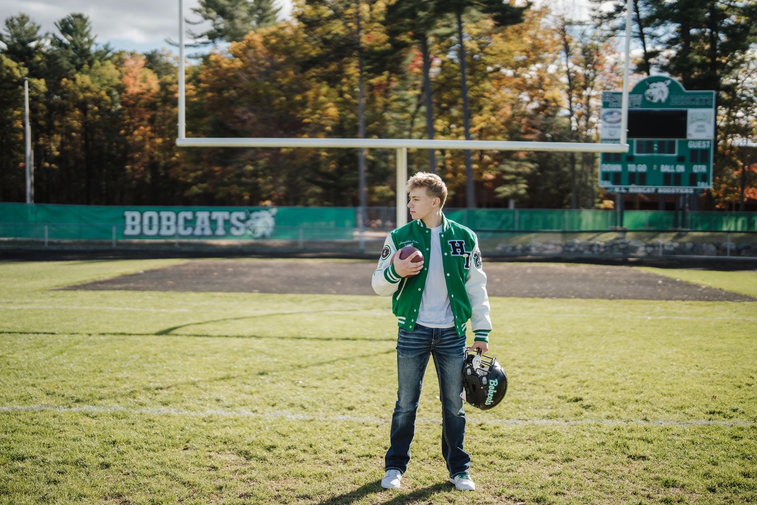 Football player stands on field holding helmet with Bobcats stadium and scoreboard in background.