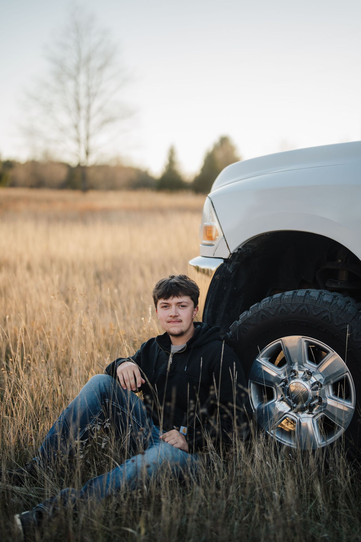 A person lies in a grassy field next to a car tire and wheel in an artistic outdoor portrait setting.