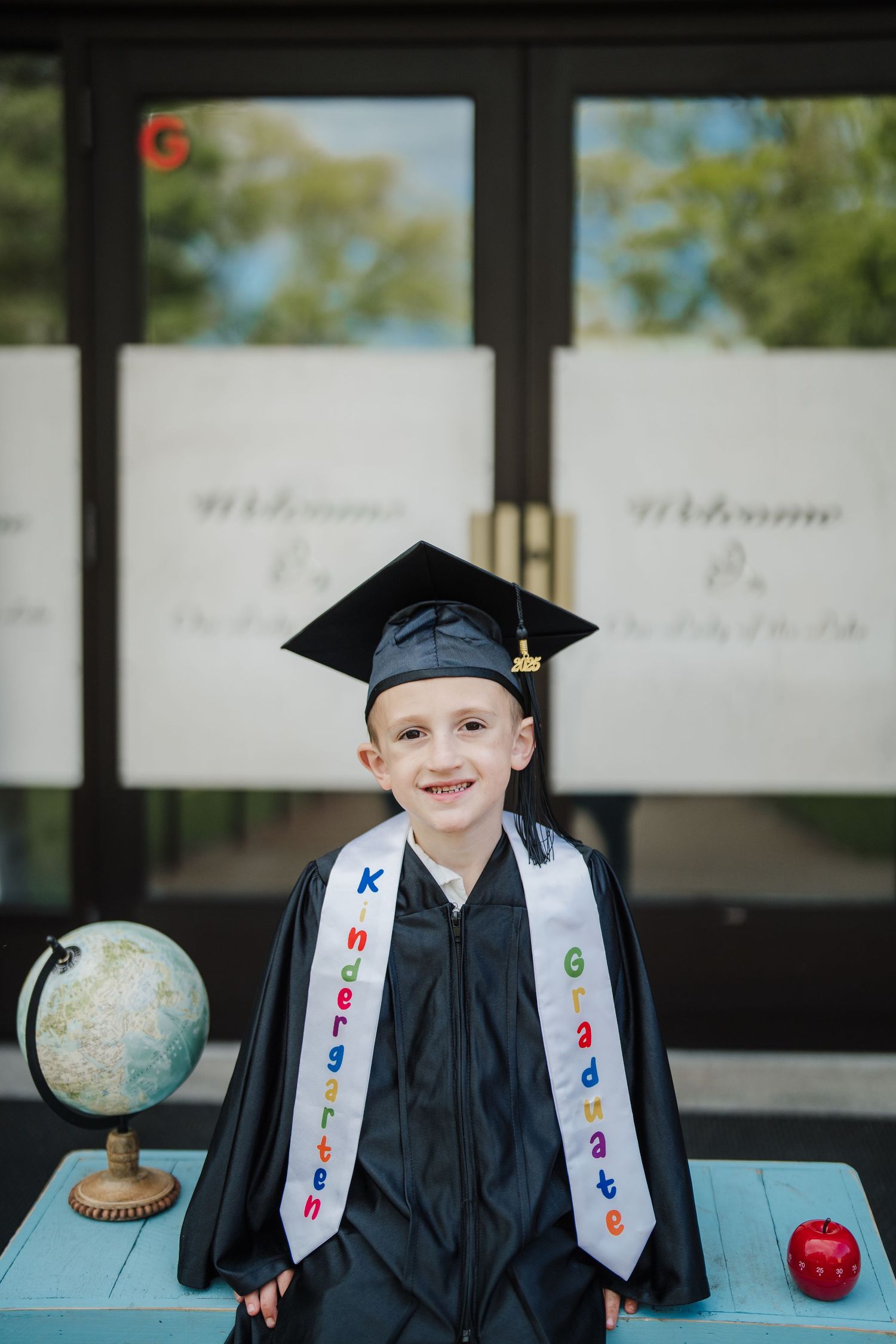 Graduate in cap and gown posing with decorative globe for graduation photos.
