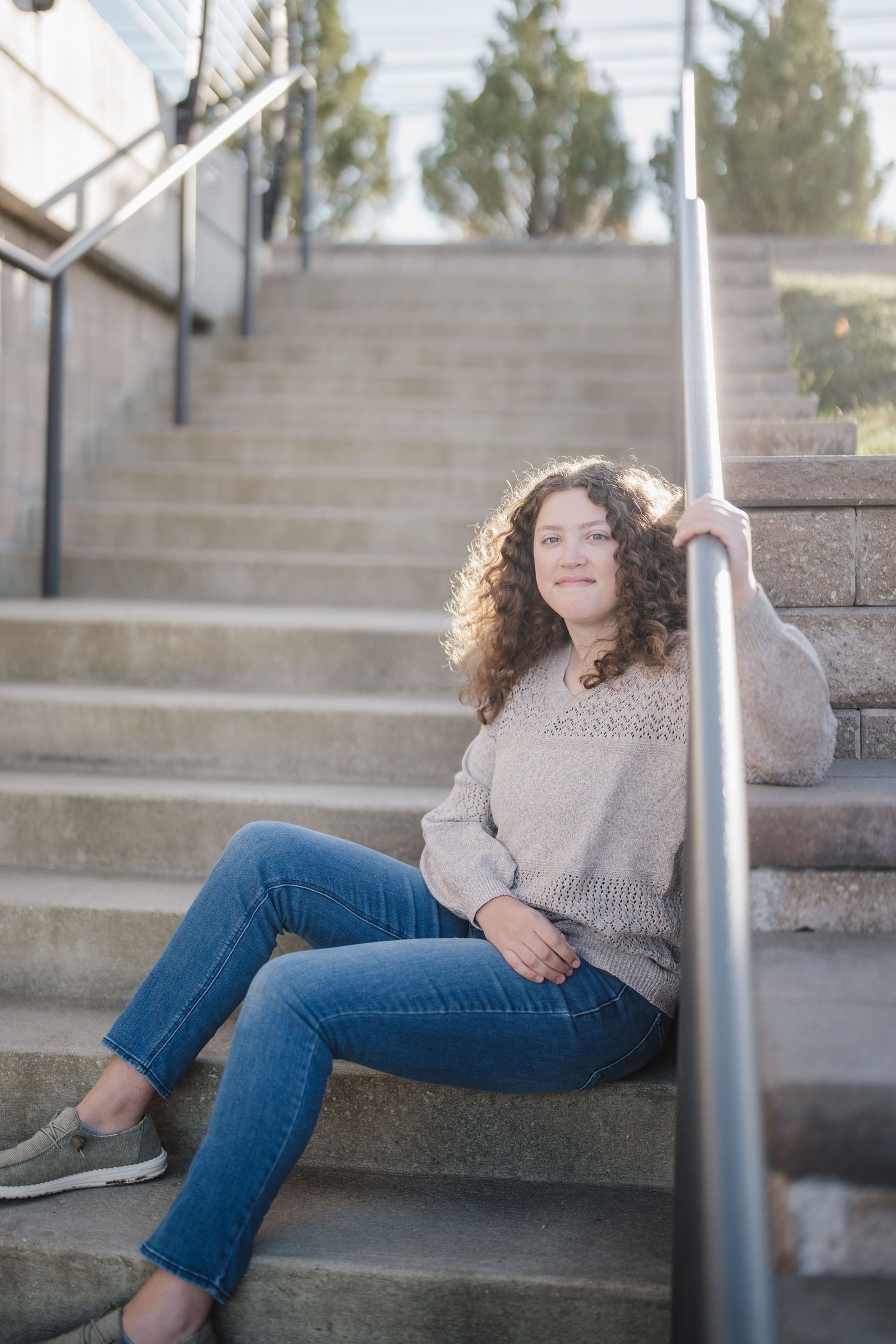 Person in beige sweater and jeans lounges casually on concrete steps outdoors in a series of relaxed poses.