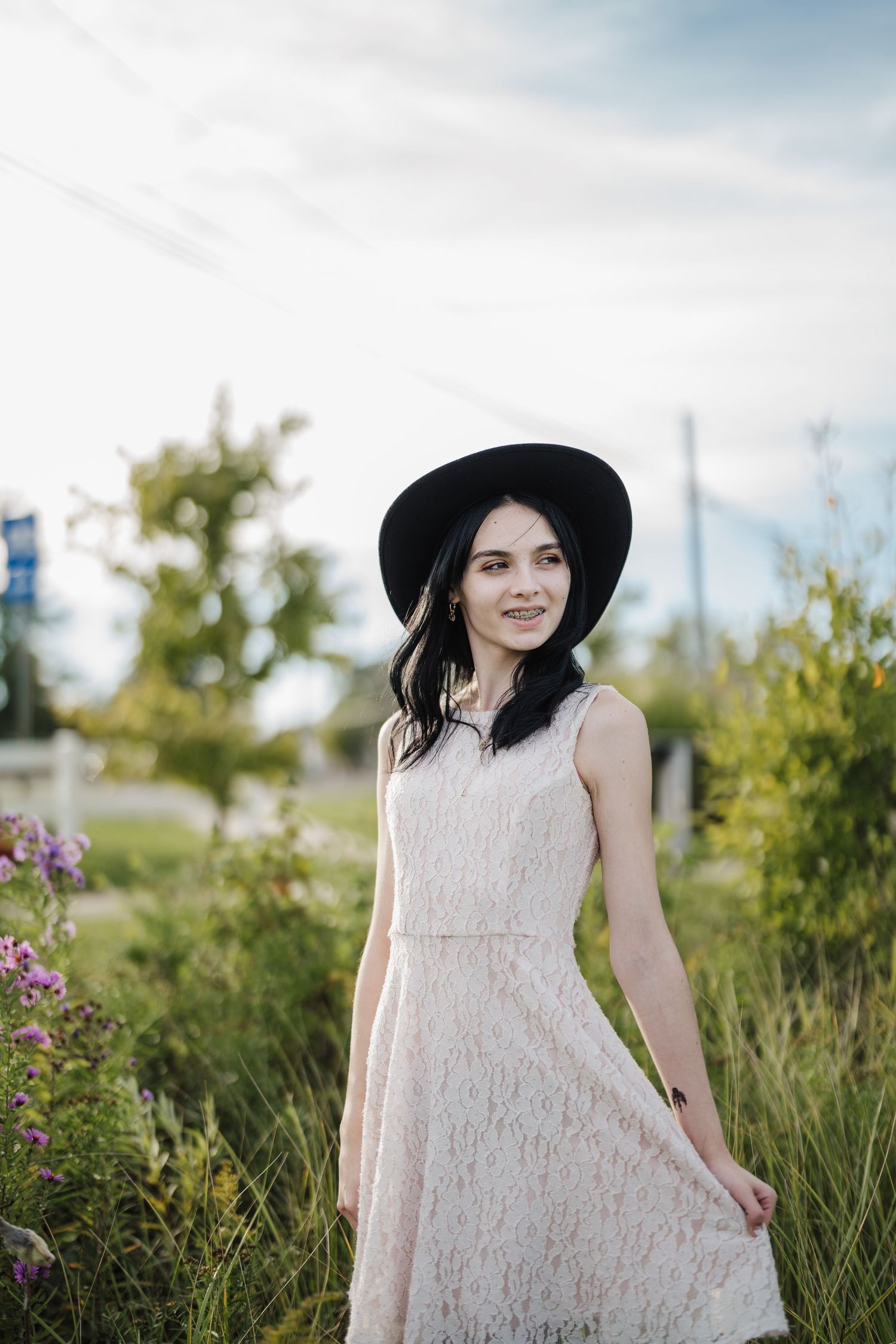 A person in a white lace dress stands among tall grass and wildflowers on a sunny summer day.