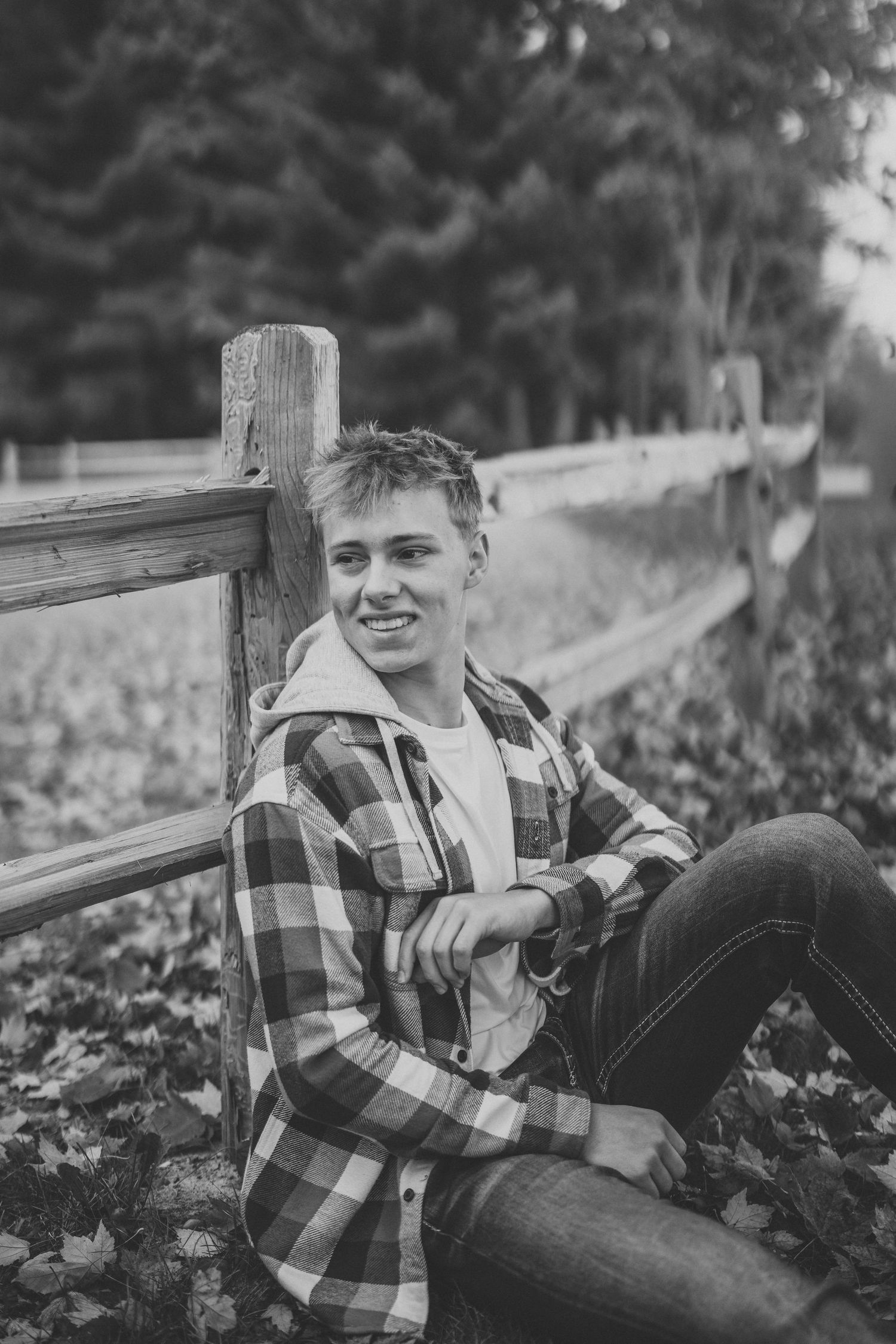 Black and white portrait series showing person in plaid flannel shirt relaxing against rustic wooden fence outdoors.