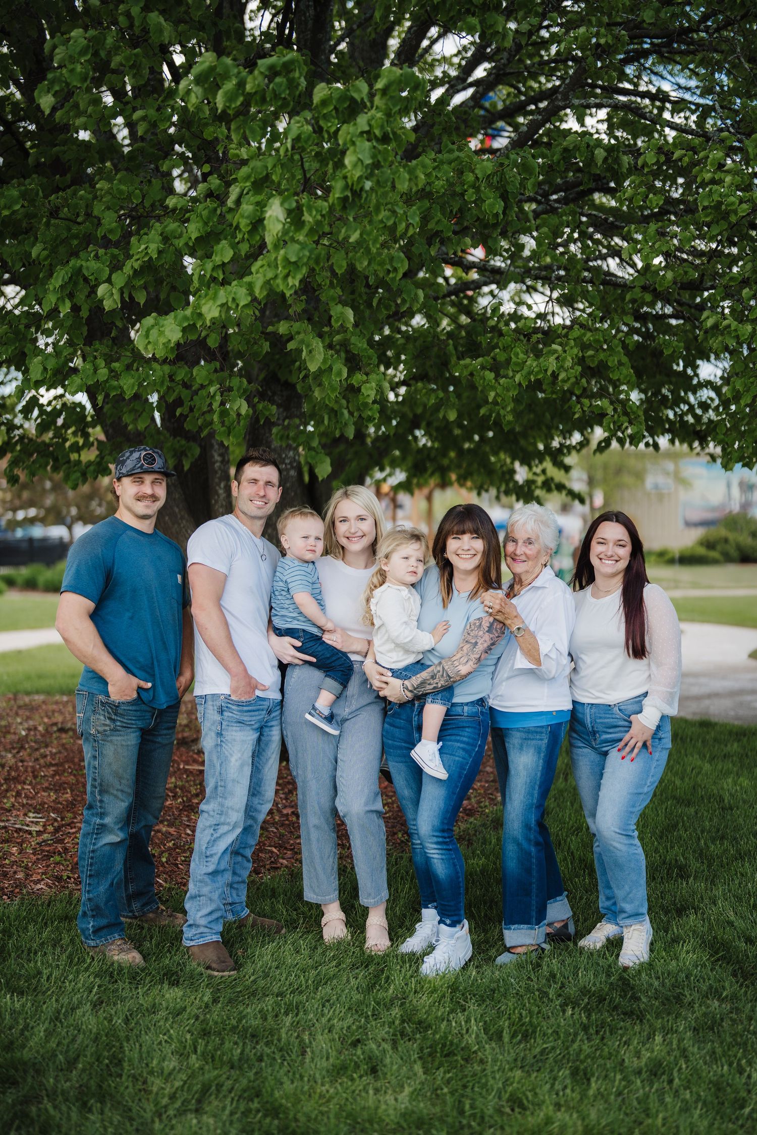 A group wearing coordinated blue and white outfits poses together on grass with trees in the background.