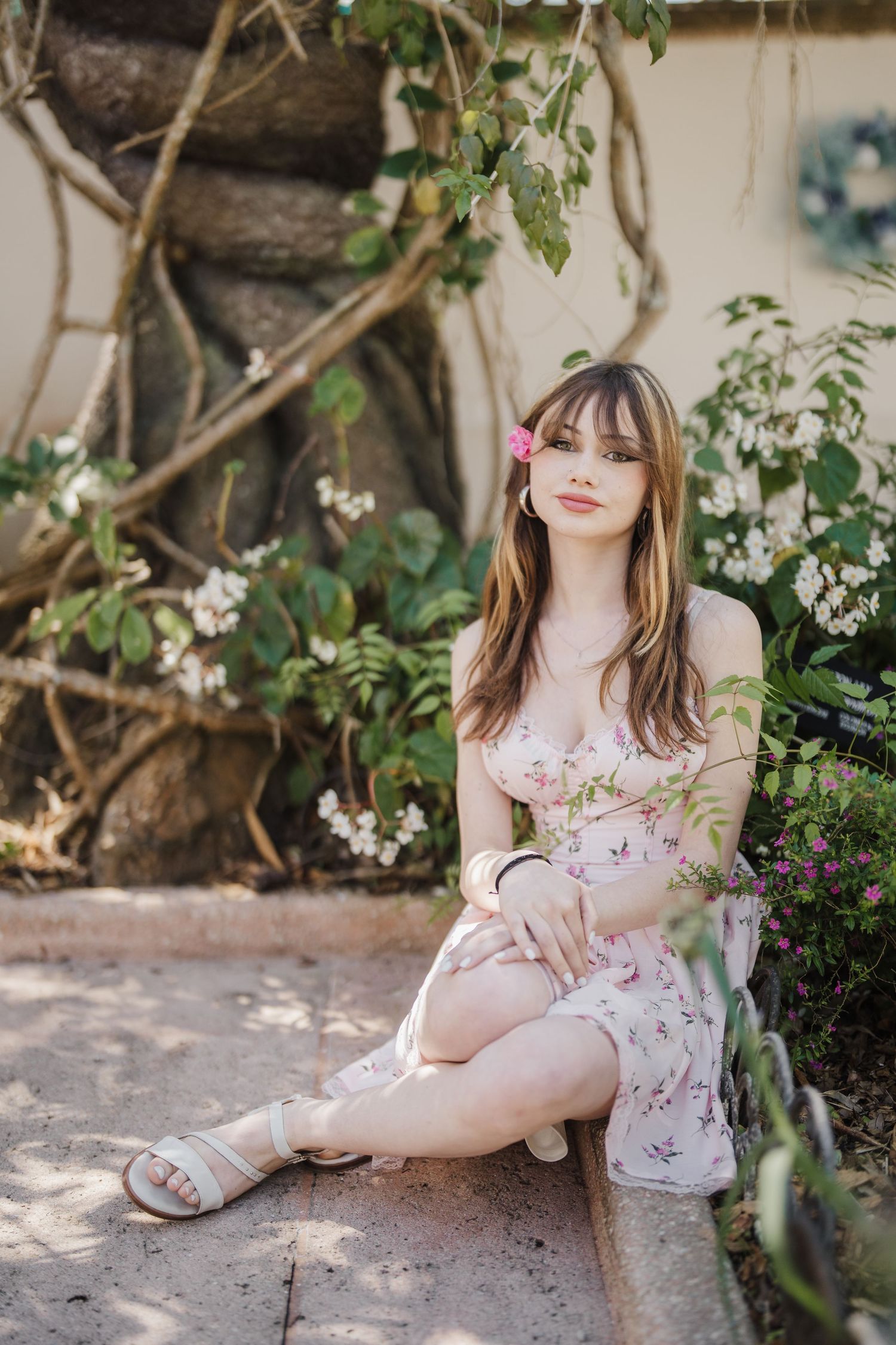 A delicate floral dress and sandals are showcased in a garden setting with dappled sunlight.