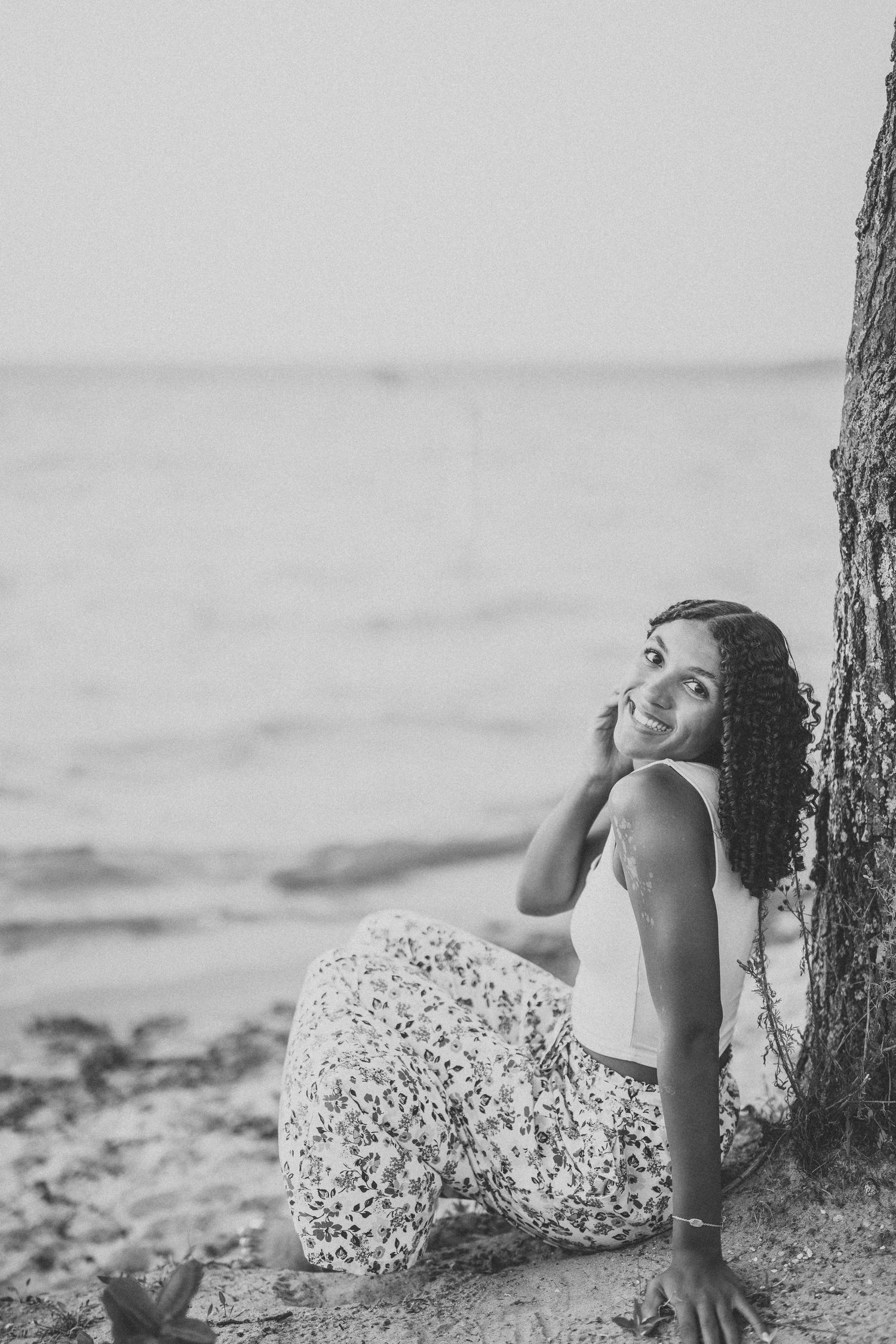 Black and white beach portraits featuring someone in a floral dress posing near driftwood on the sand.