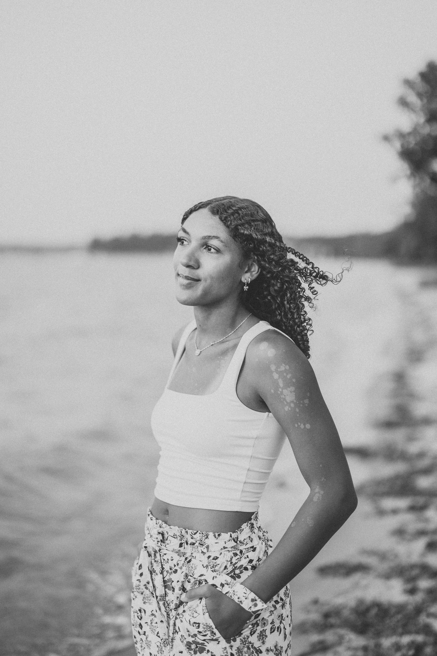 A person in a white crop top and floral skirt poses against a bright, overexposed beach background.