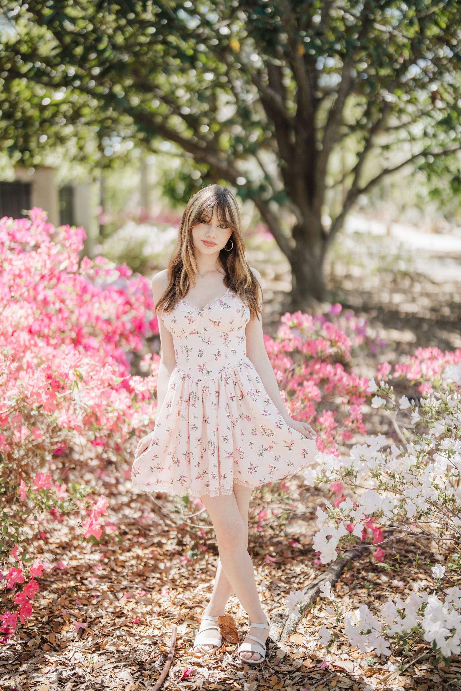 A dreamy spring photoshoot in a garden with blooming pink azaleas and white flowers under dappled sunlight.