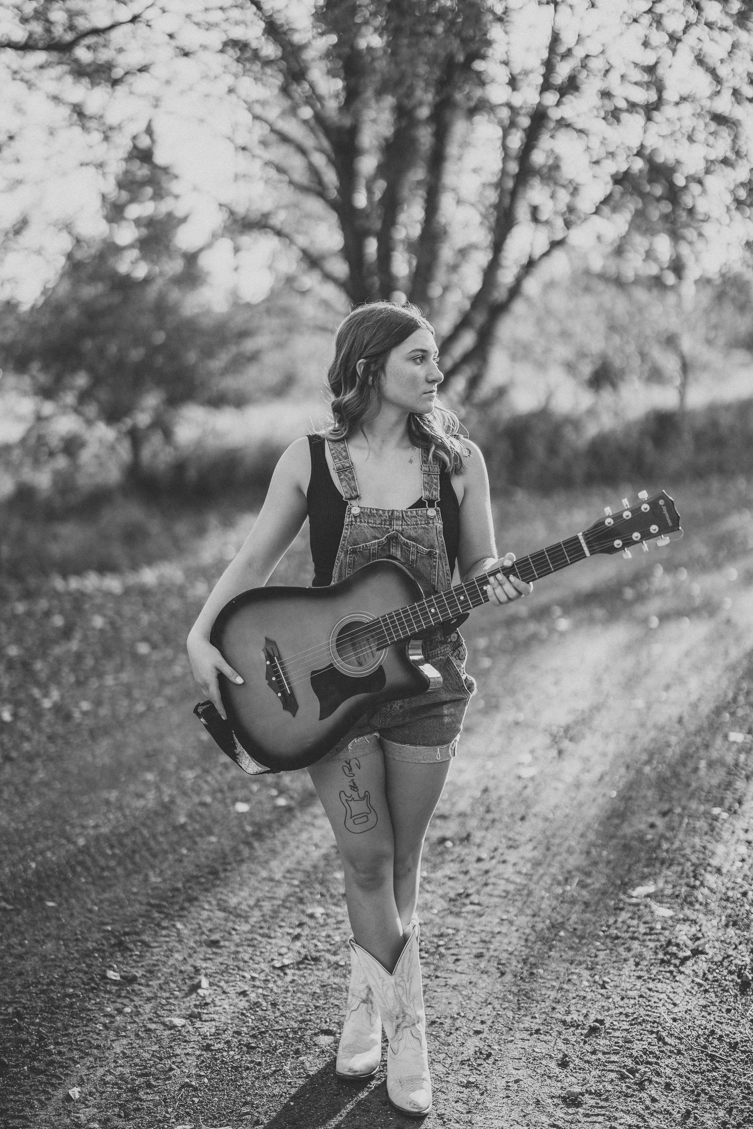 Black and white portrait of musician with guitar on rural dirt path.